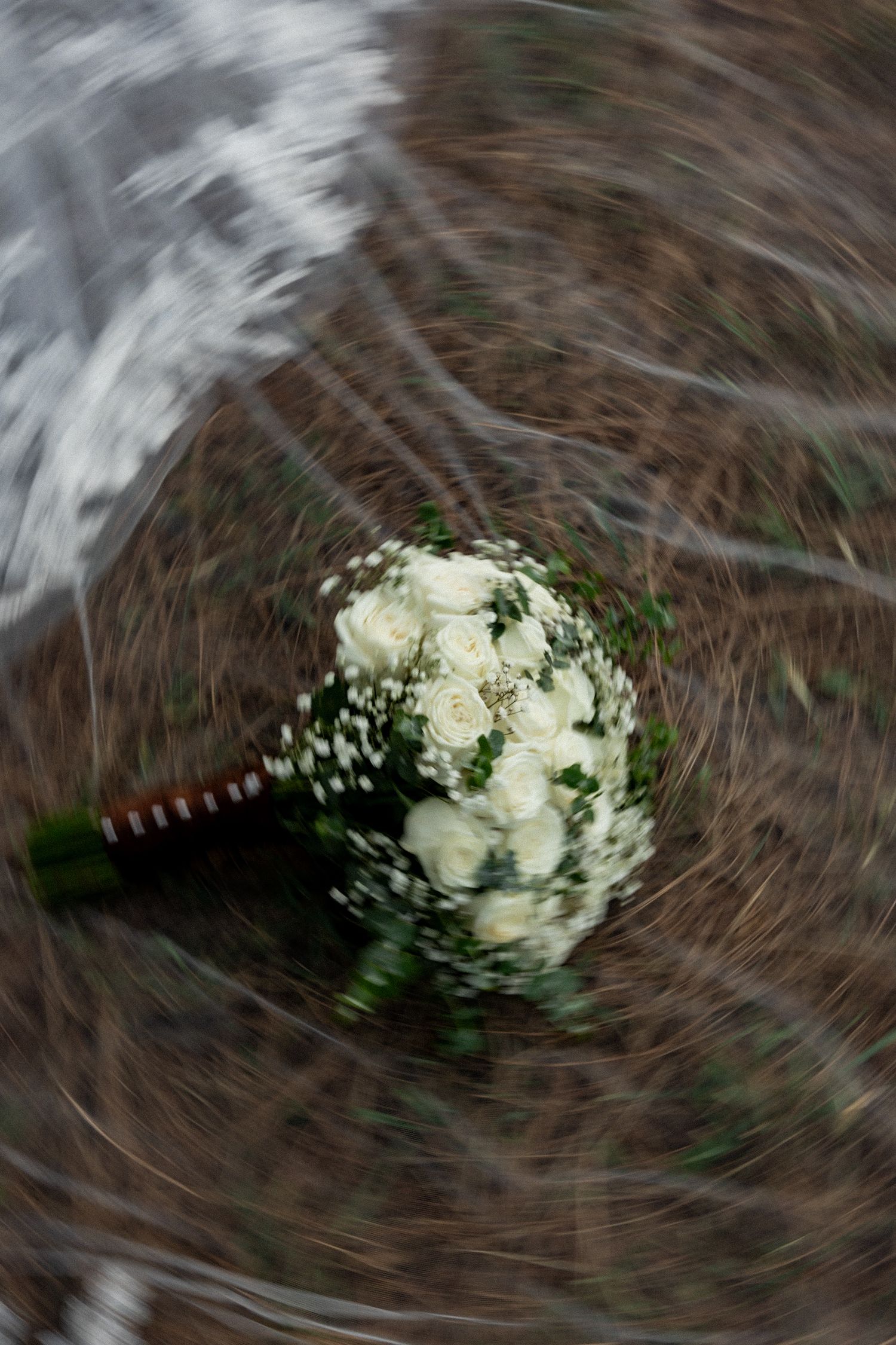A bridal bouquet of white roses with a swirling motion blur effect, placed on a natural ground.