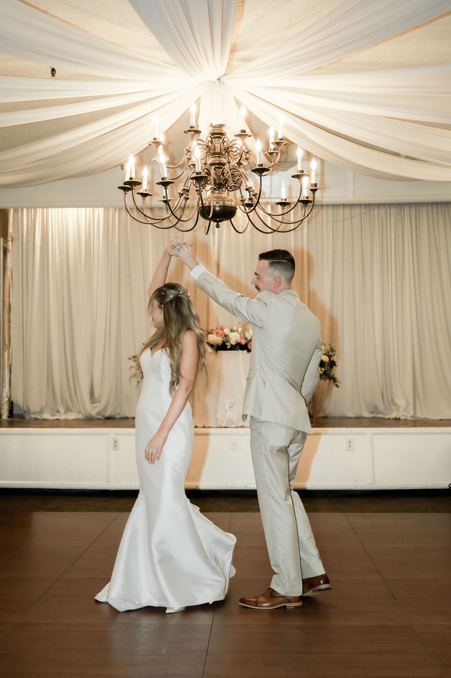 Newlyweds dancing in an elegant white tent reception venue with chandelier lighting.