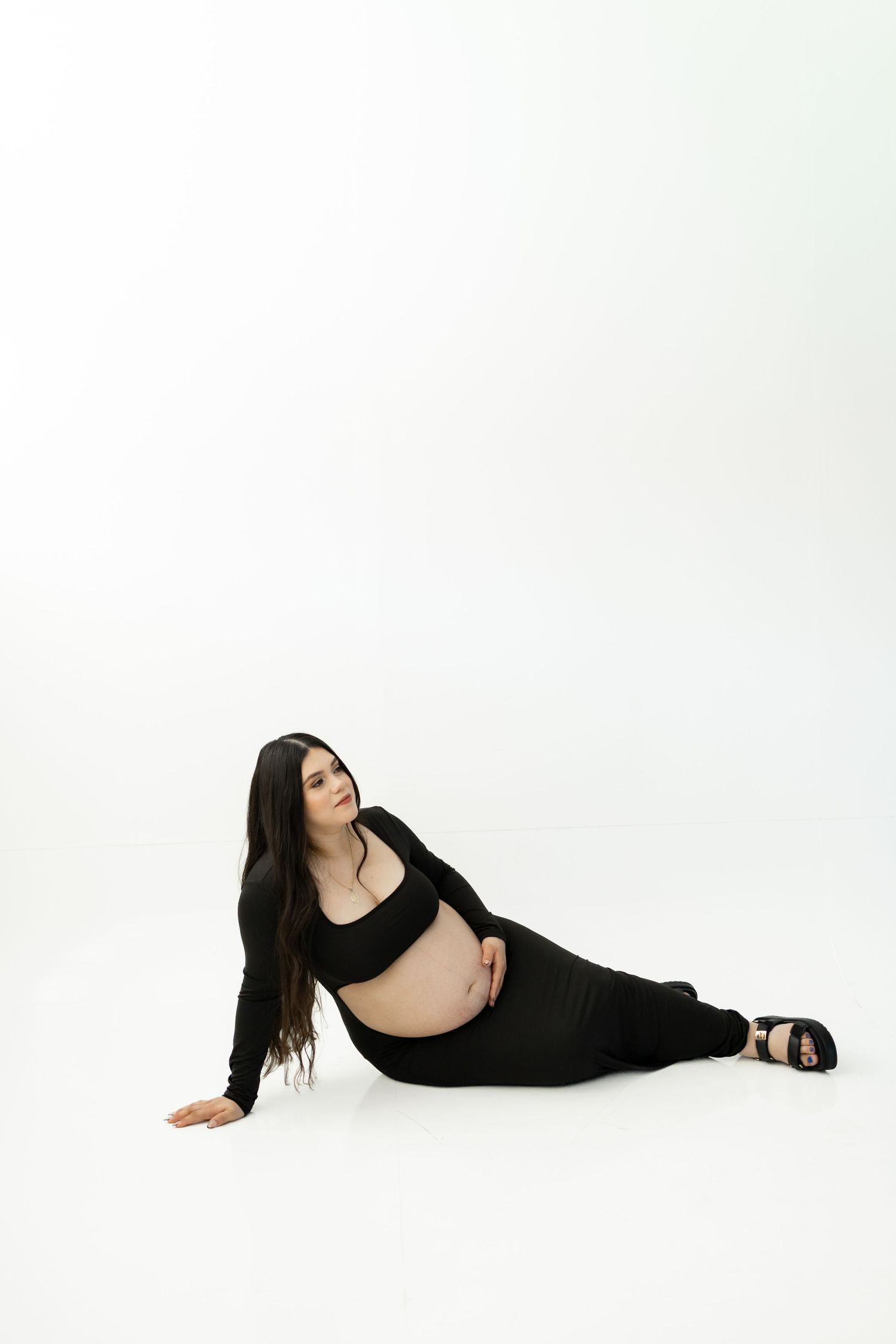A person in black athletic wear poses gracefully on a white backdrop during a minimalist photoshoot.