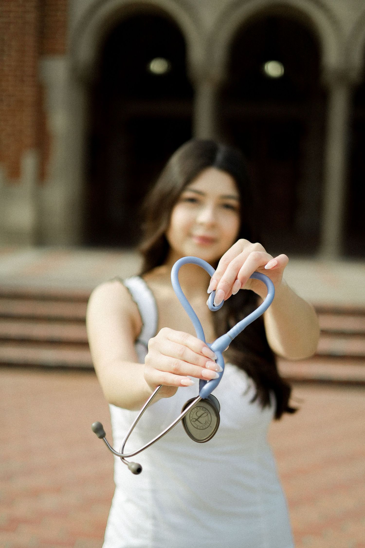 A sequence of hands demonstrating how to tie a blue ribbon in a bow against a blurred brick background.