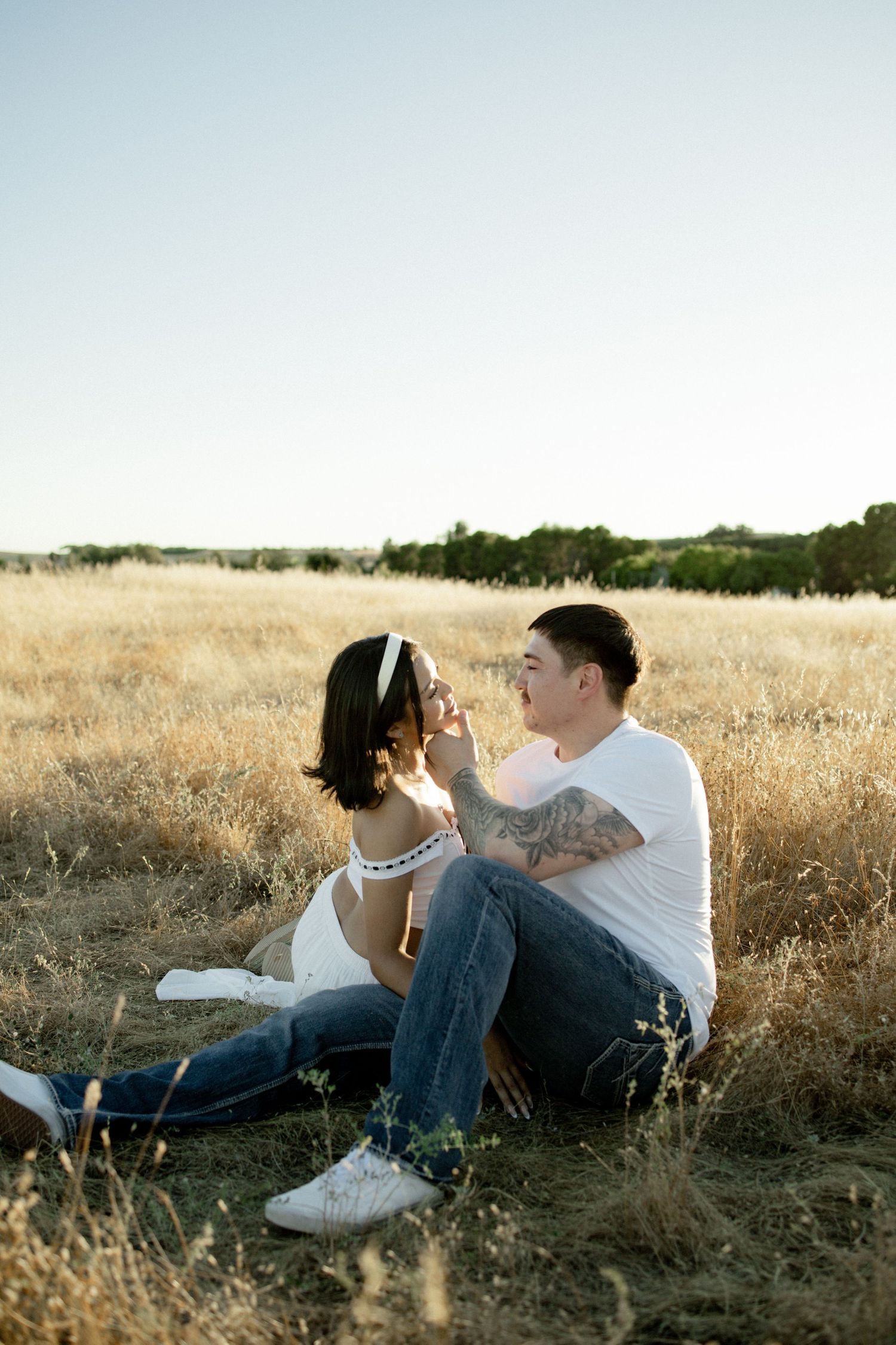 Couple relaxing together in golden sunlit field during casual engagement photo session.