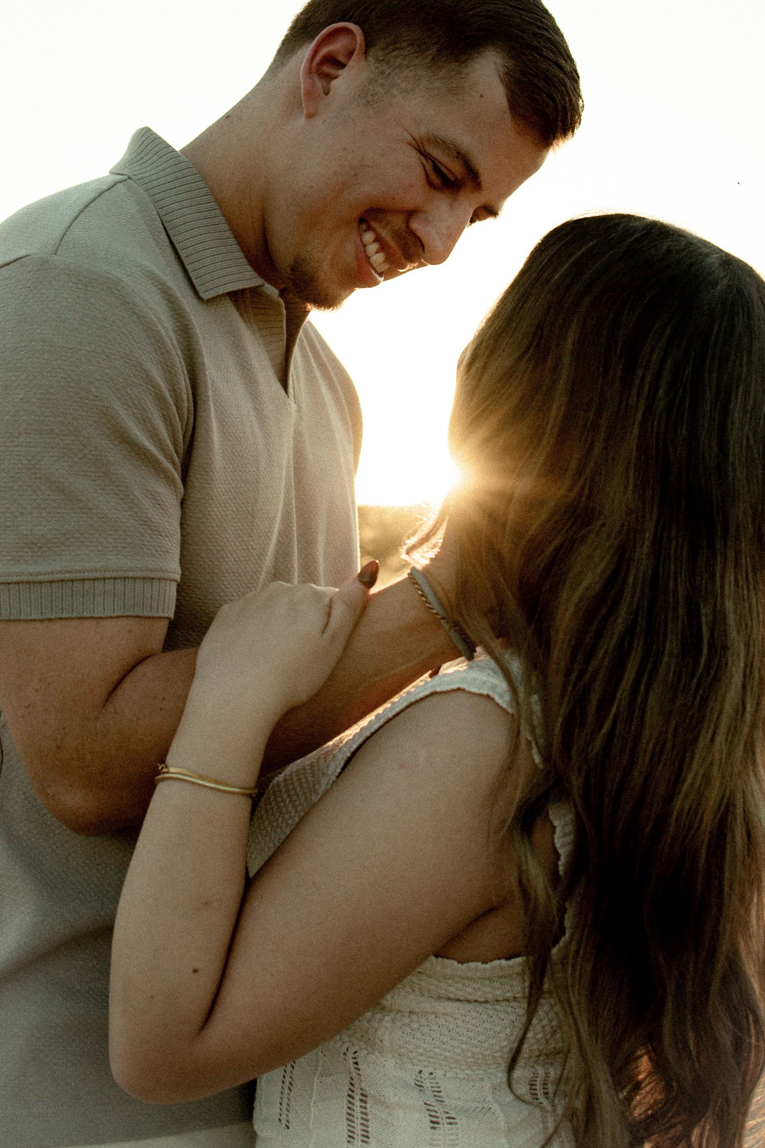 A romantic couple shares an intimate moment at sunset with golden light streaming between them.