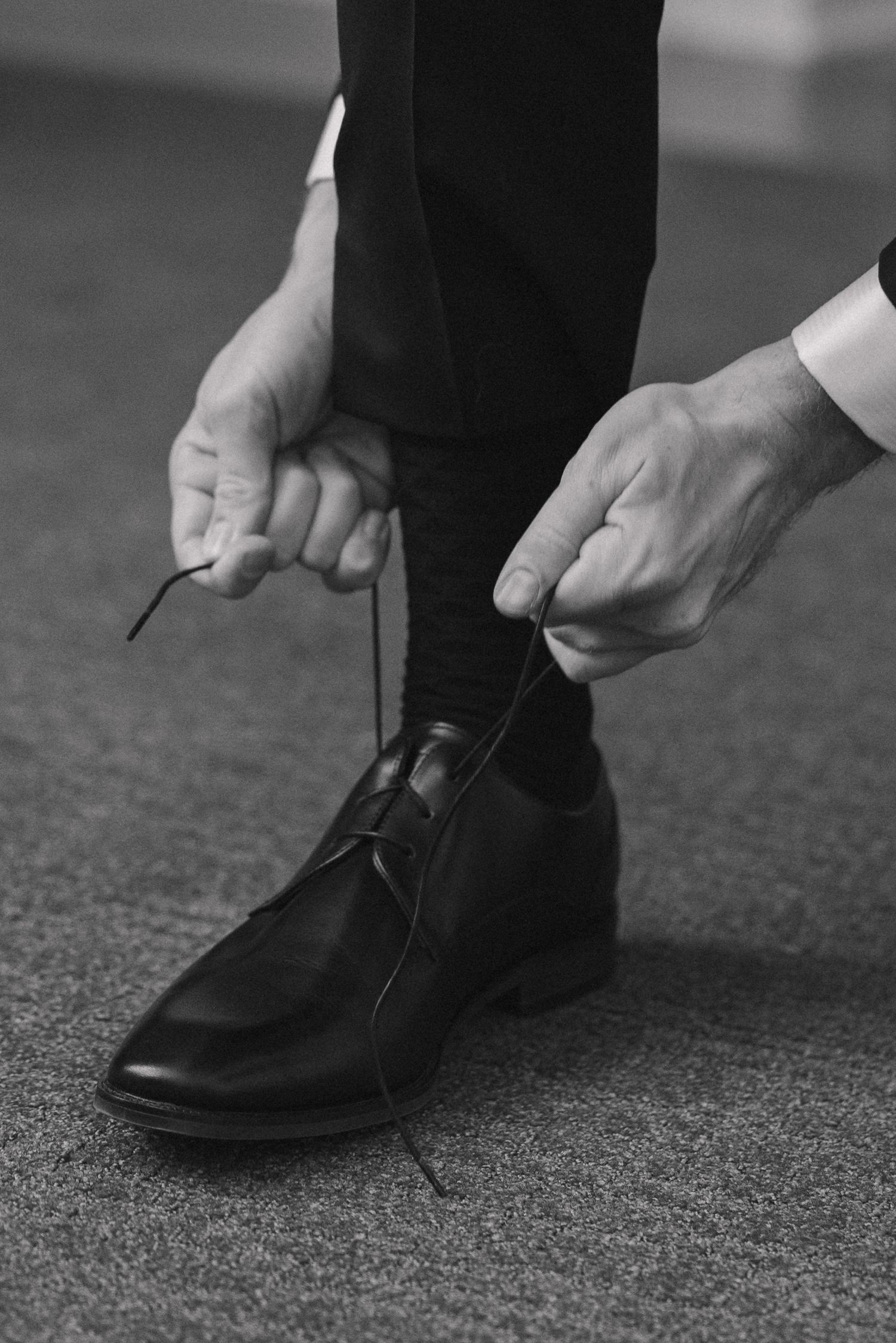 Black and white close-up of a groom tying his dress shoe laces before his wedding ceremony.