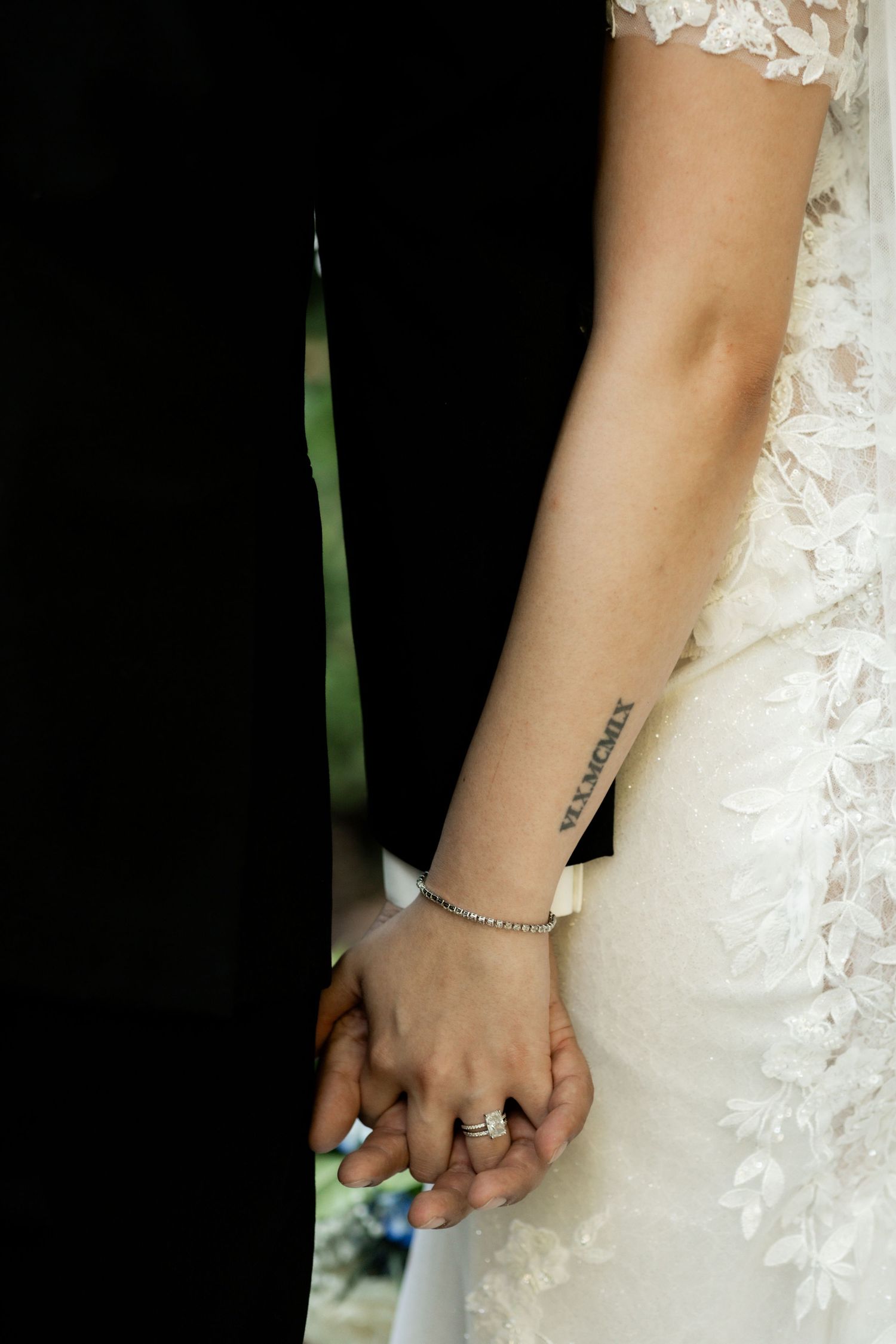 Close-up detail of lace wedding dress and bridal jewelry against dark background.