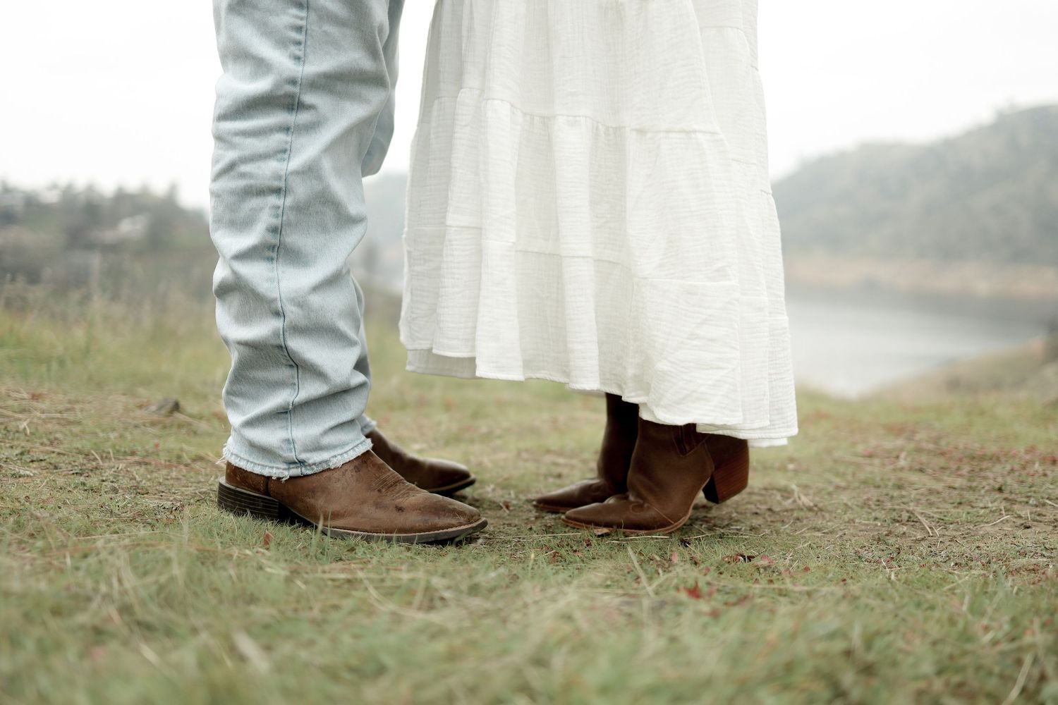 Close-up view of feet standing together on grass showing brown leather shoes and white dress.