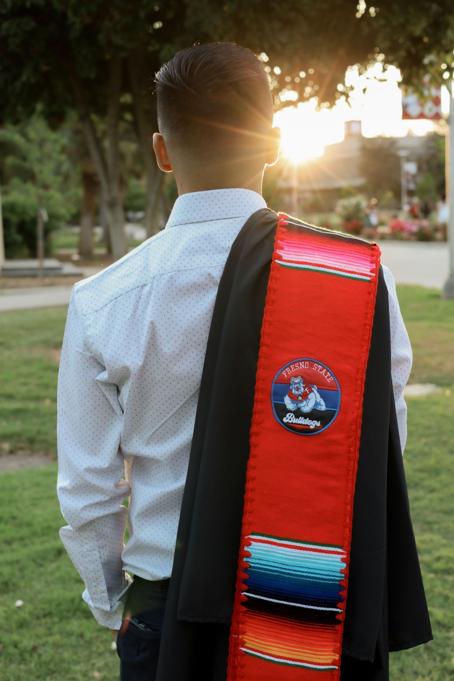 A person wearing a white dress shirt and black vest with a colorful serape-style blanket in sunset lighting.