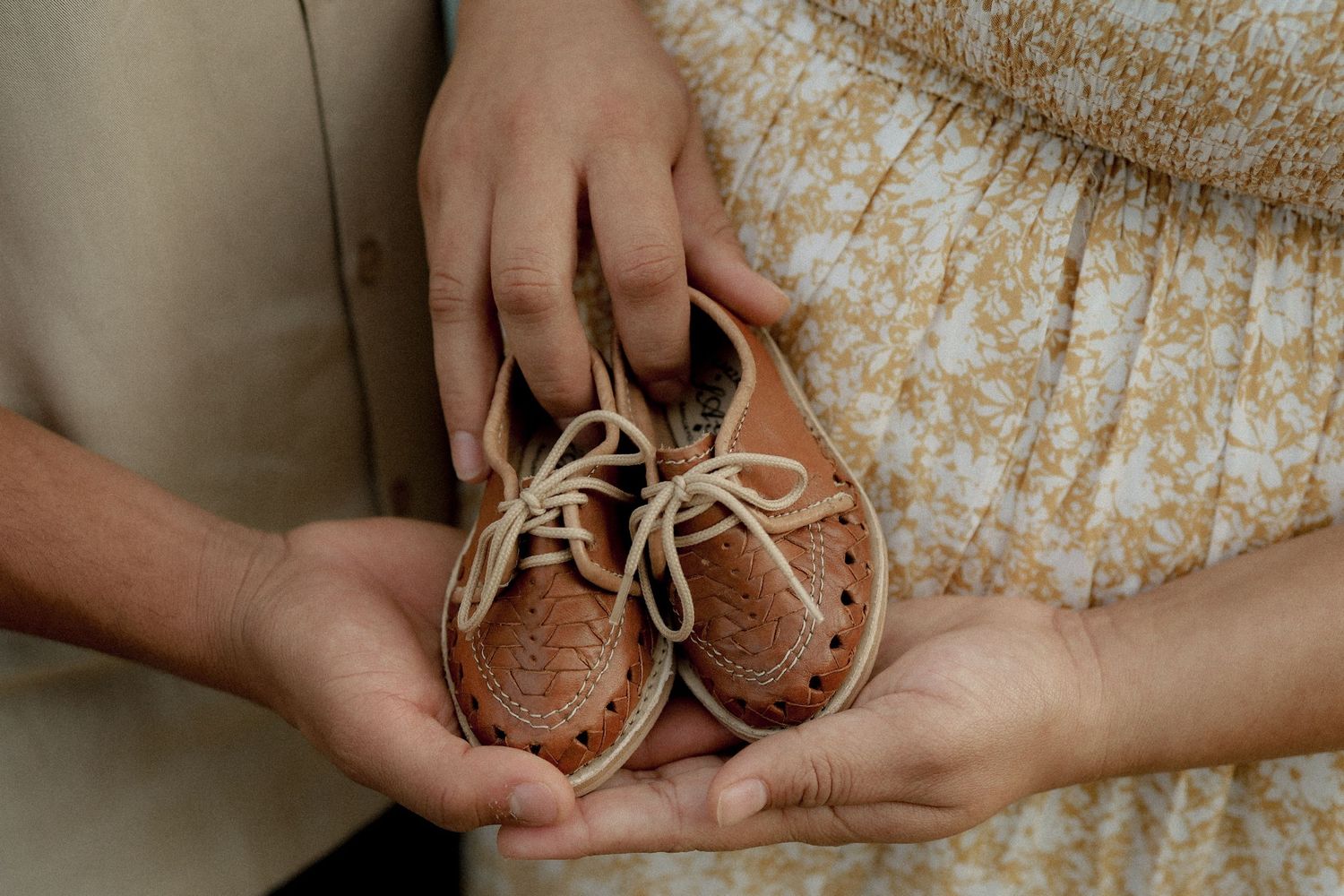A series of hands holding small brown leather baby shoes in a progression of different angles and poses.