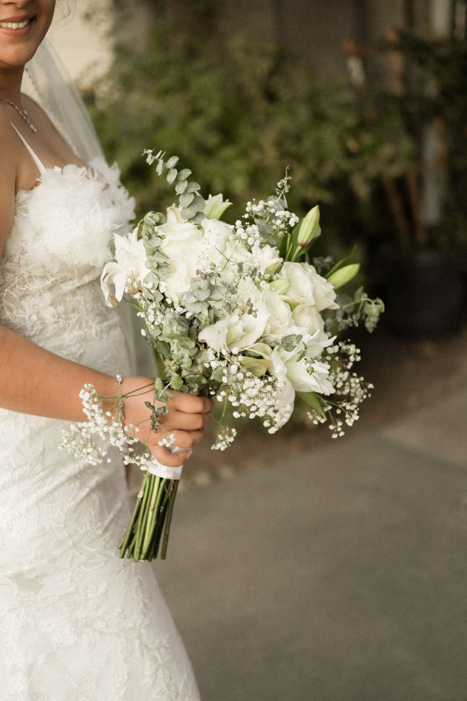 An elegant white bridal bouquet with lilies and baby's breath held by someone in a wedding dress.