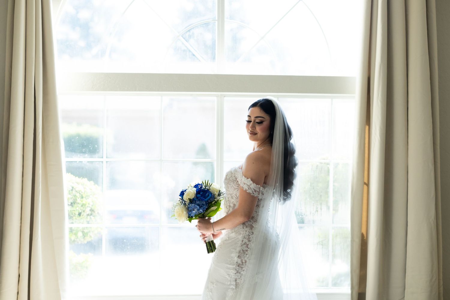 Wedding dress silhouette against bright window with flowing curtains.