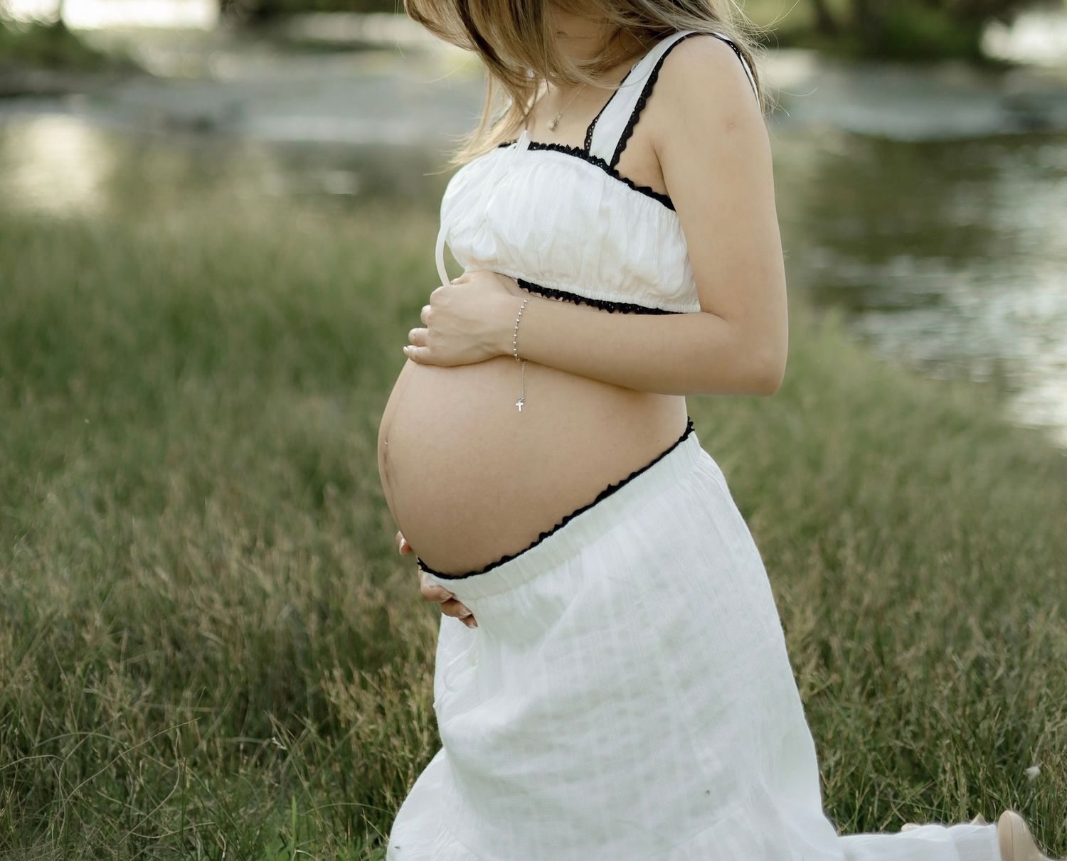 A progression of maternity photos showing a growing baby bump in a white dress by a lake.