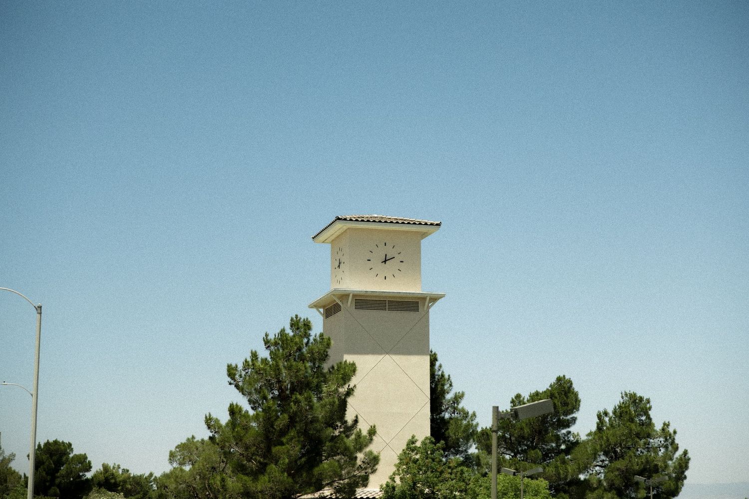 A tall white clock tower rises above green trees against a clear blue sky.