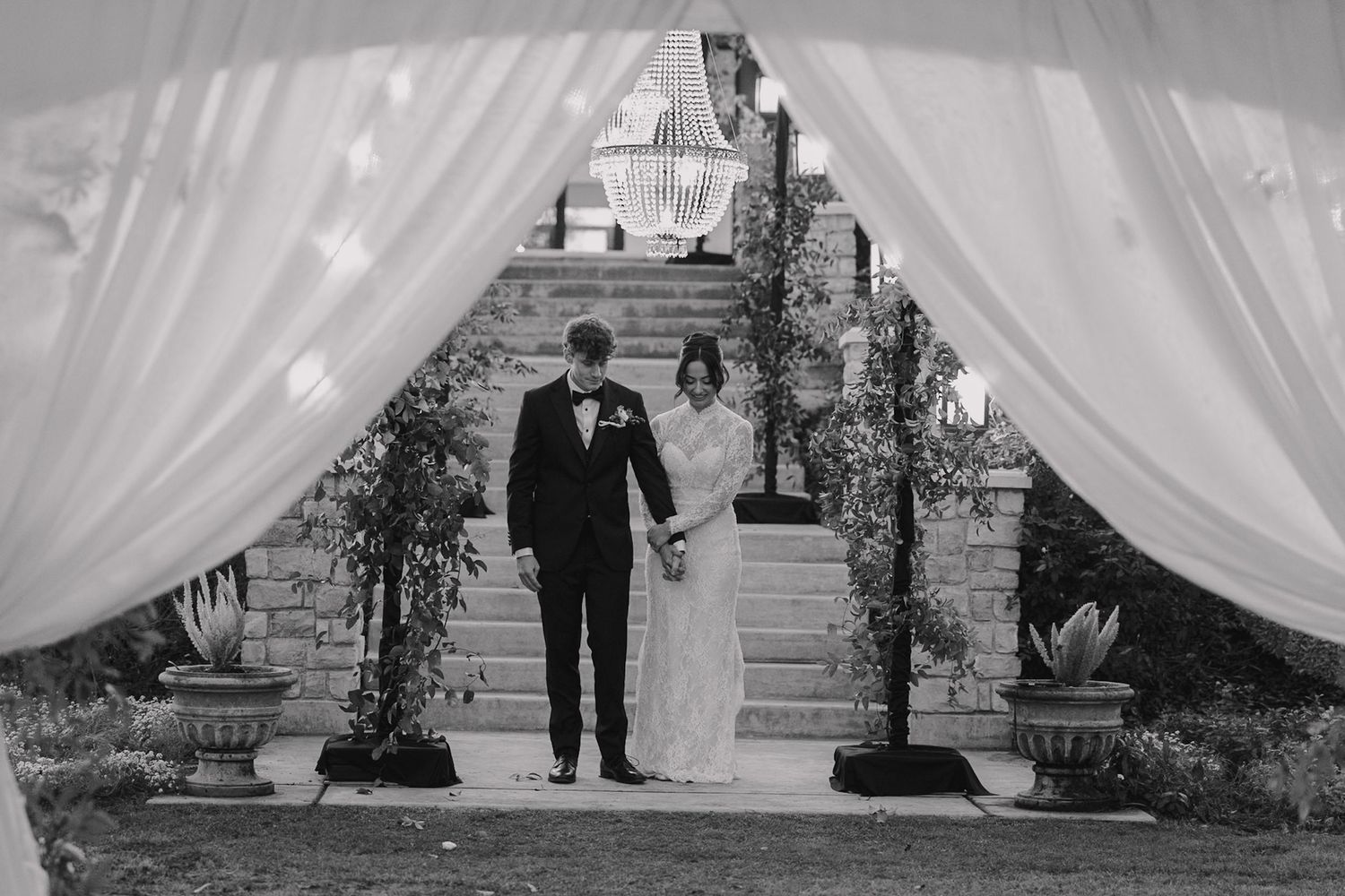Black and white photo of bride and groom walking through white draped wedding ceremony exit.