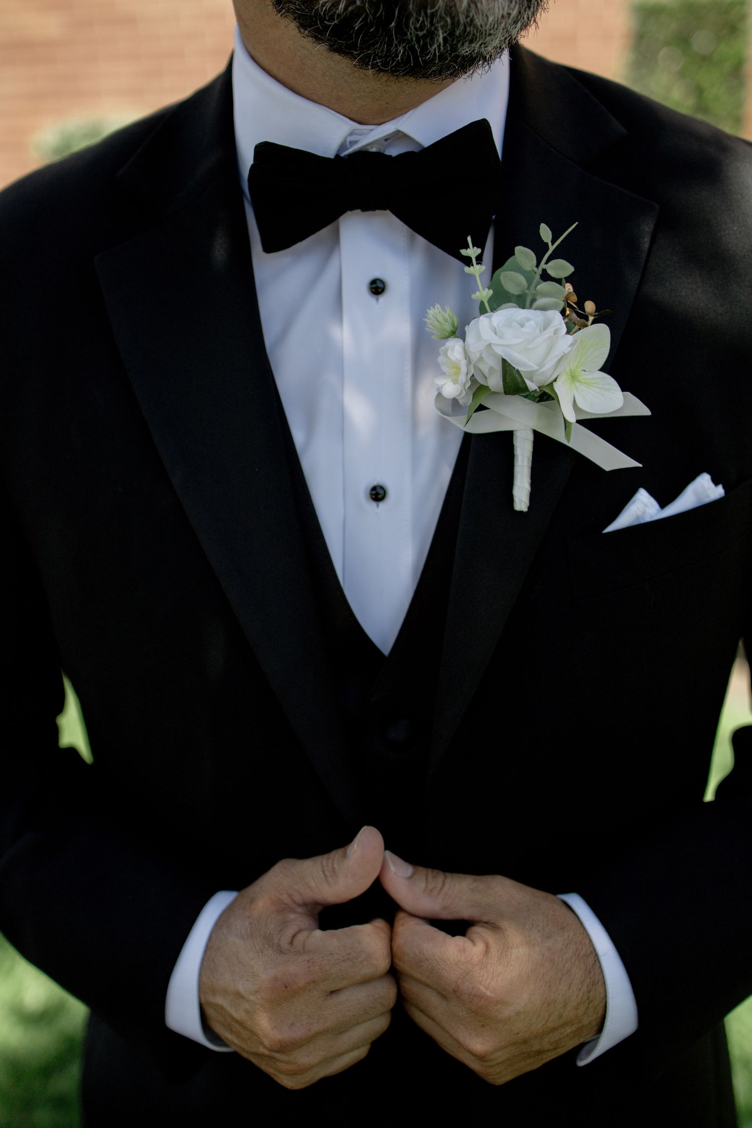 Close-up details of groom's formal black tuxedo with white boutonniere and bow tie.