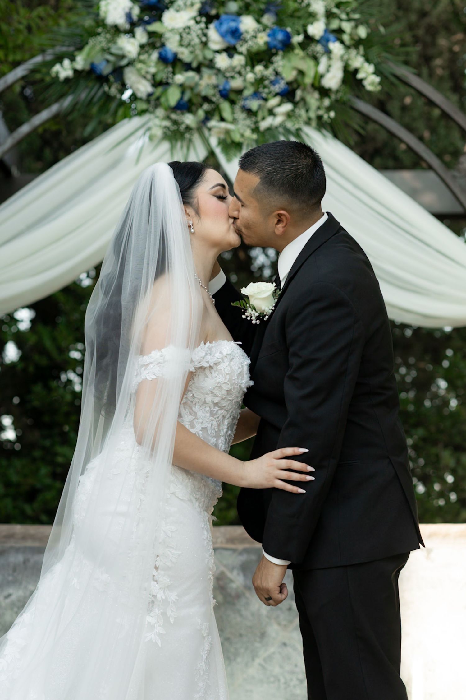 A romantic wedding ceremony moment under an elegant white draped canopy with floral decorations.