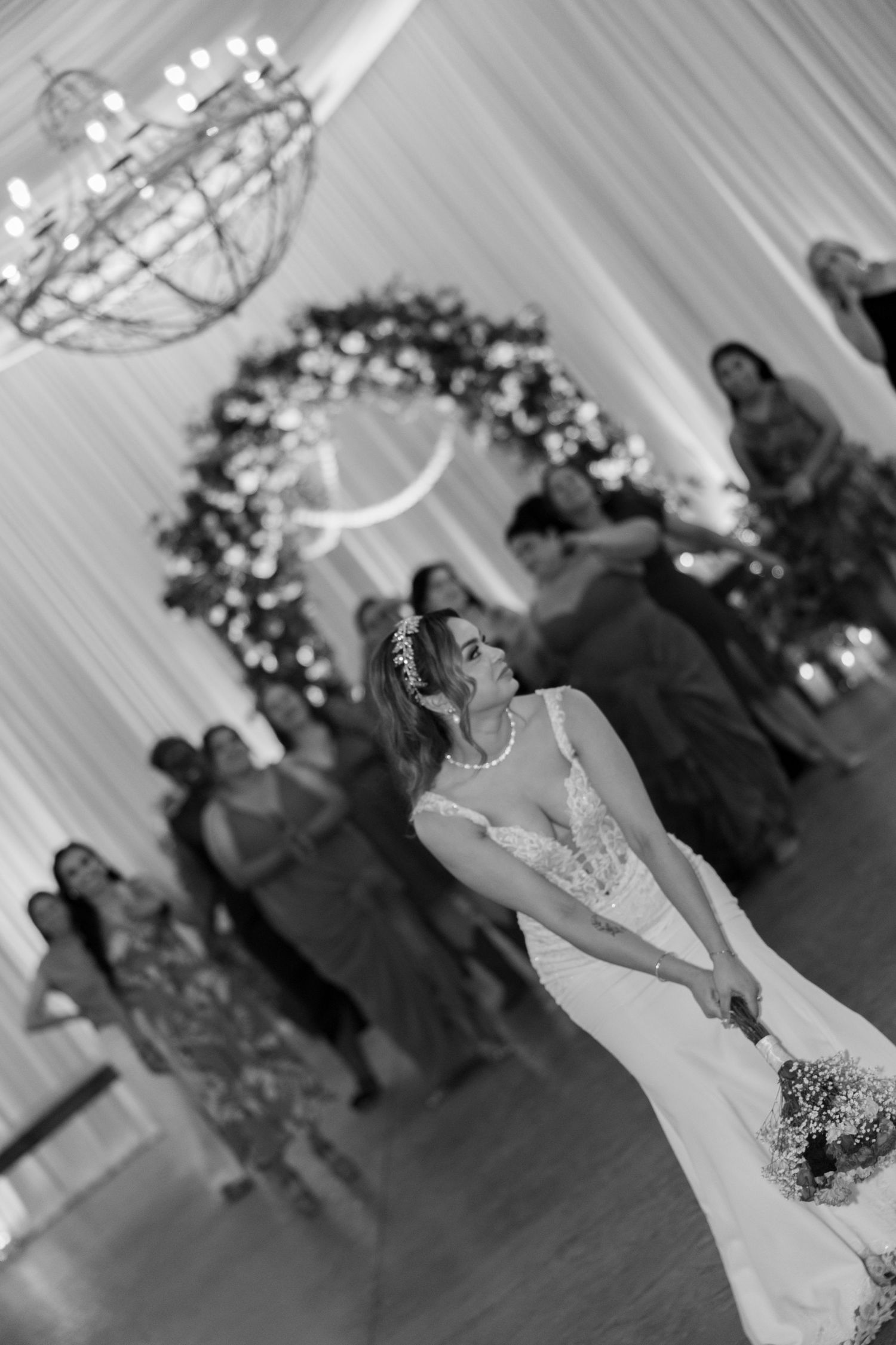 Bride in white gown tosses bouquet to guests at elegant wedding reception in black and white photo.