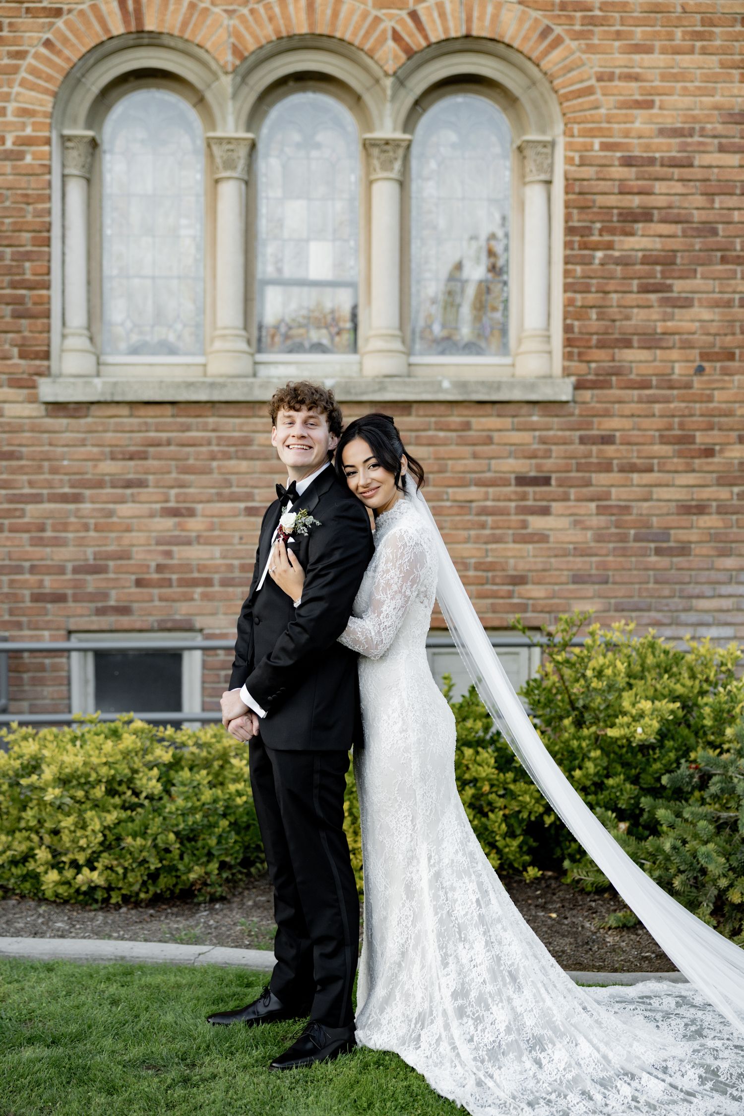 A couple shares a joyful moment together outside a brick church building on their wedding day.