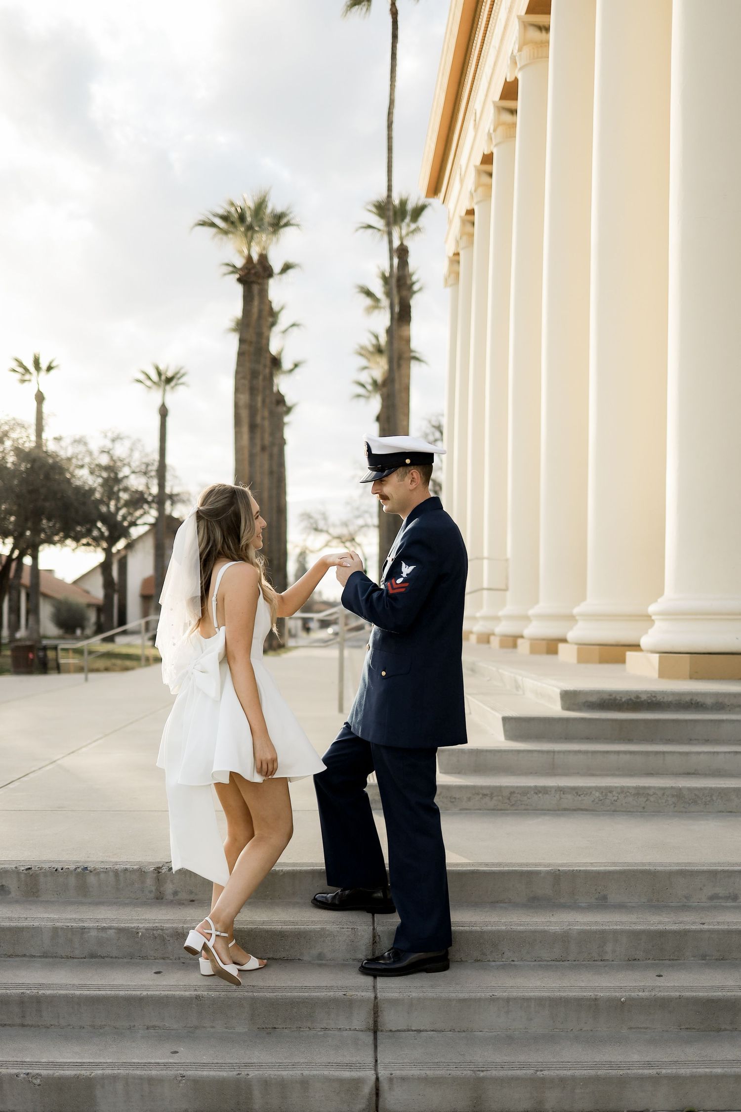 Sequence showing interaction on white columned steps with palm trees in background.