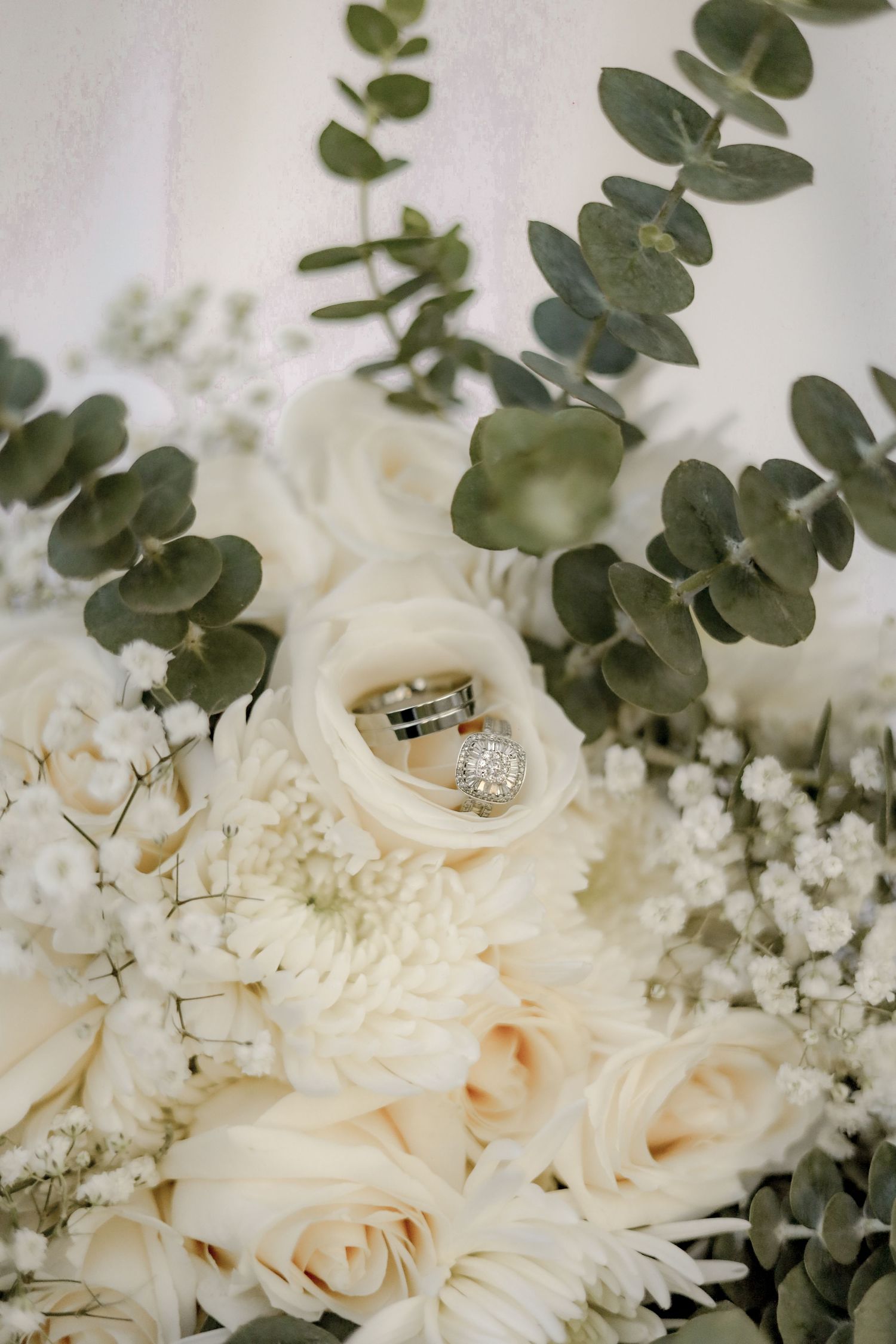 White roses and eucalyptus leaves arranged with wedding rings in an elegant bridal bouquet.