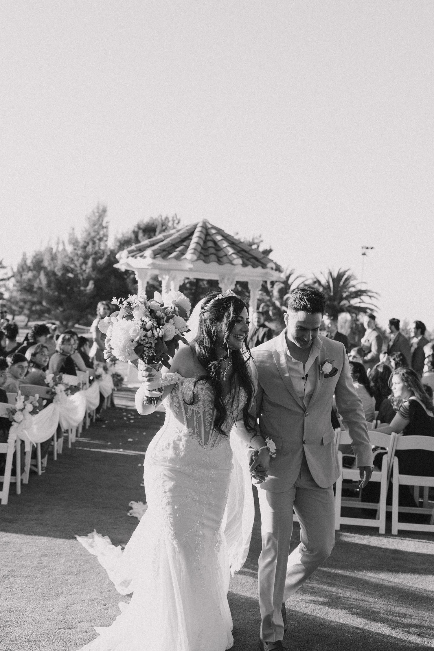 Black and white photo of a bride and groom walking down the aisle after their outdoor wedding ceremony.