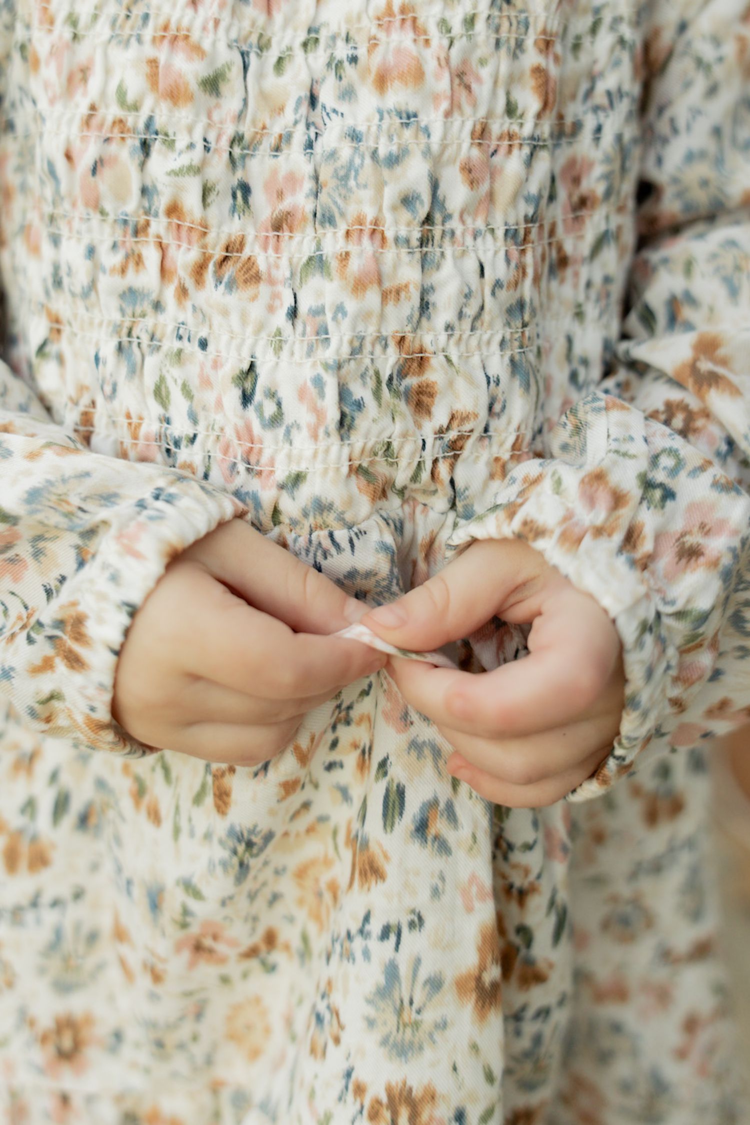 Close-up of hands holding delicate fabric with a soft floral pattern in peach and green tones.