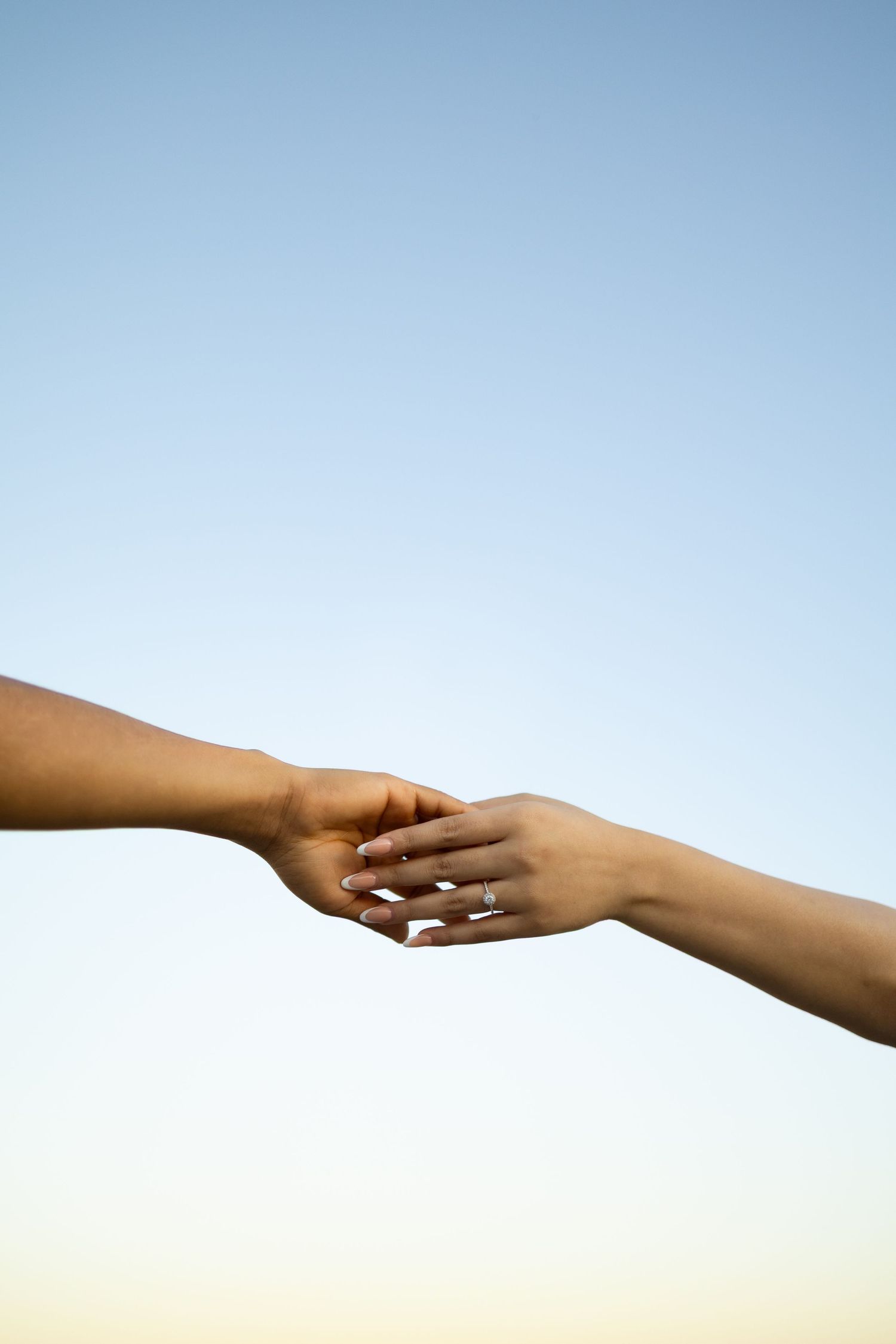 Two hands reaching towards each other against a bright blue sky background.