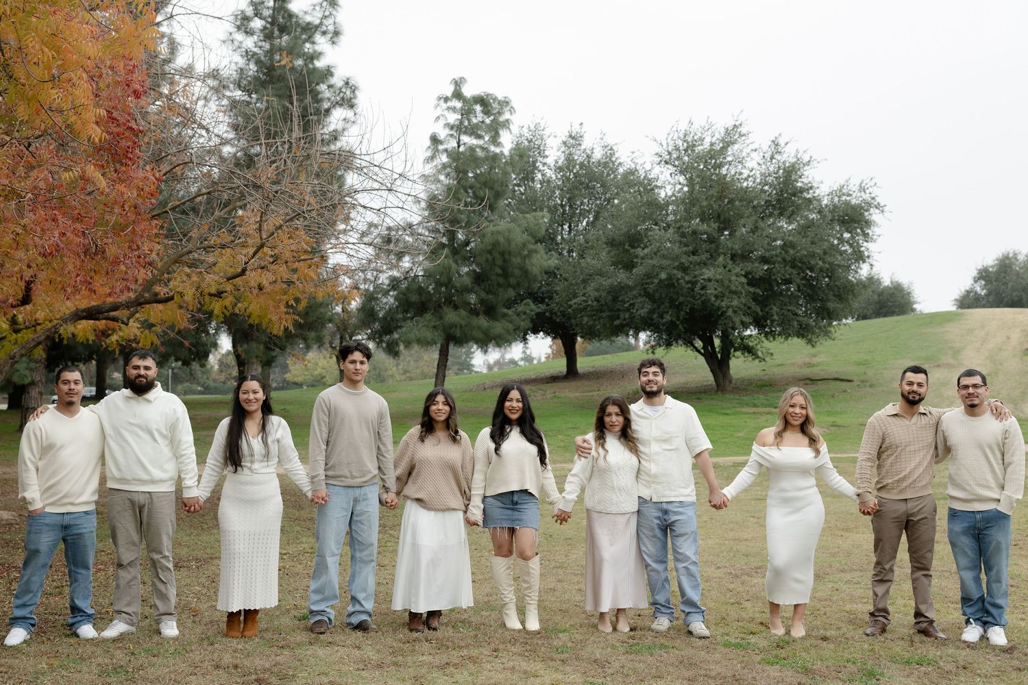 A group of people in casual attire standing in a line outdoors during autumn with colorful fall foliage in the background.