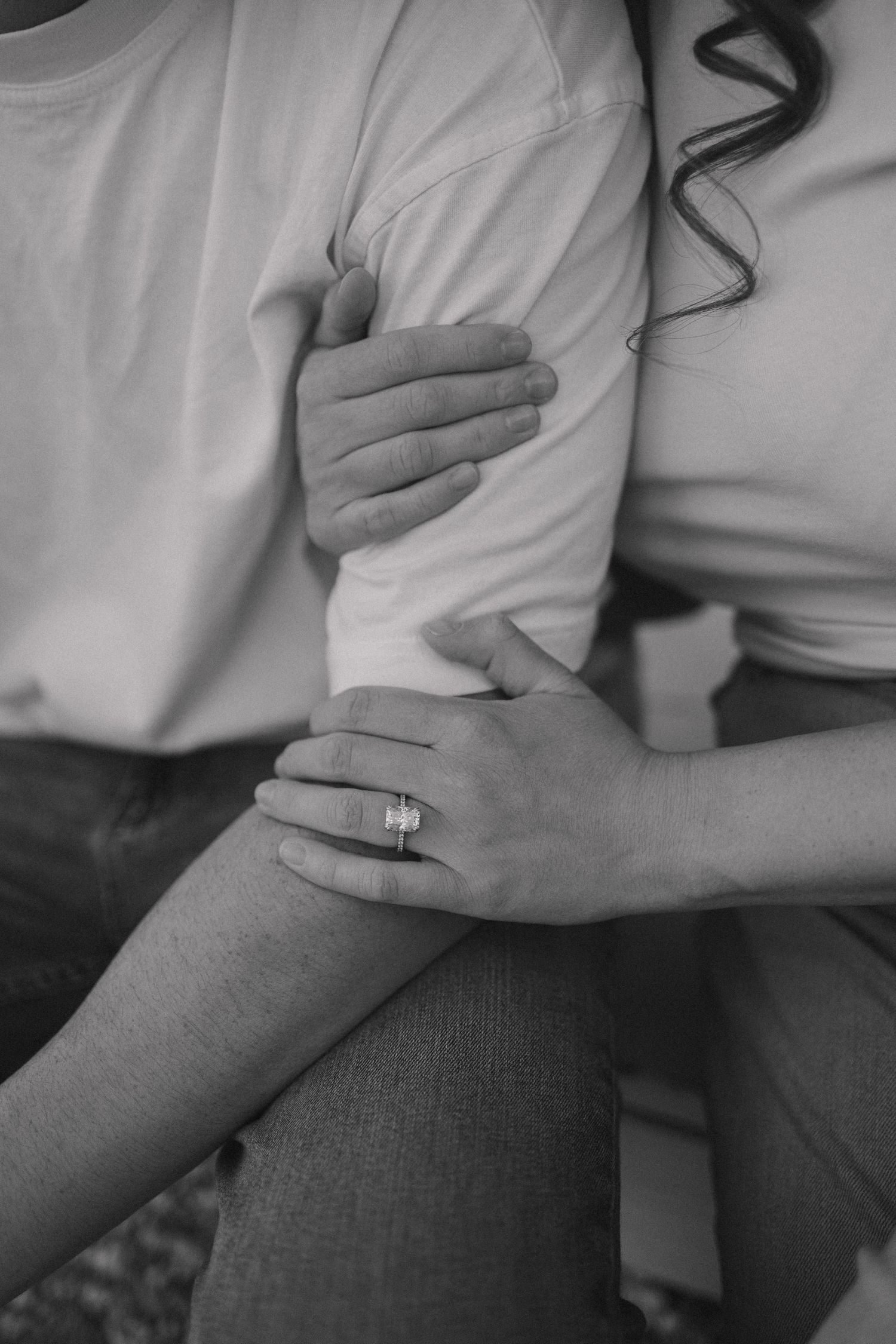 Close-up black and white photo showing hands embracing with a wedding ring visible.