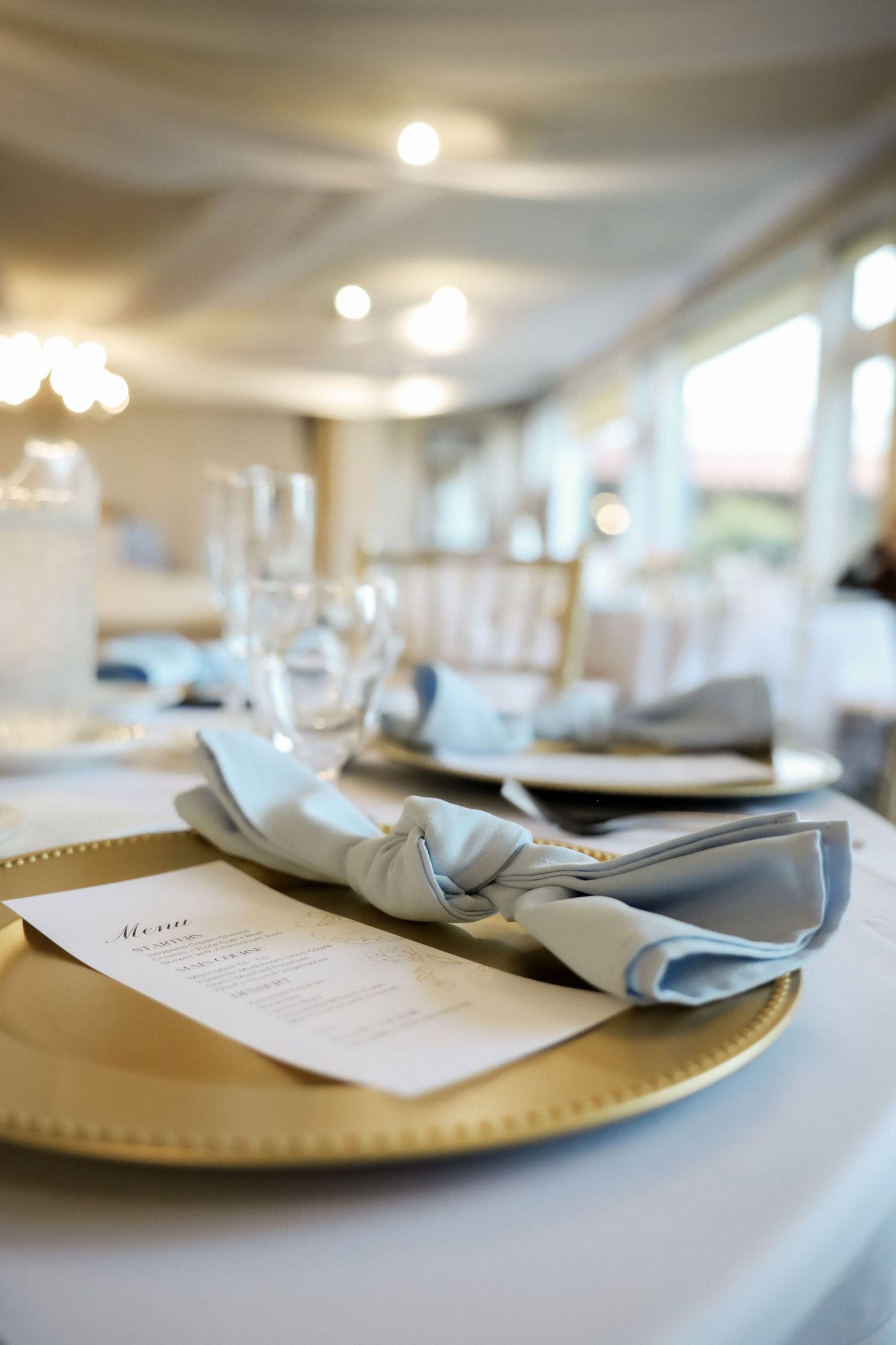 Elegant place settings with gold chargers and blue napkins at wedding reception.