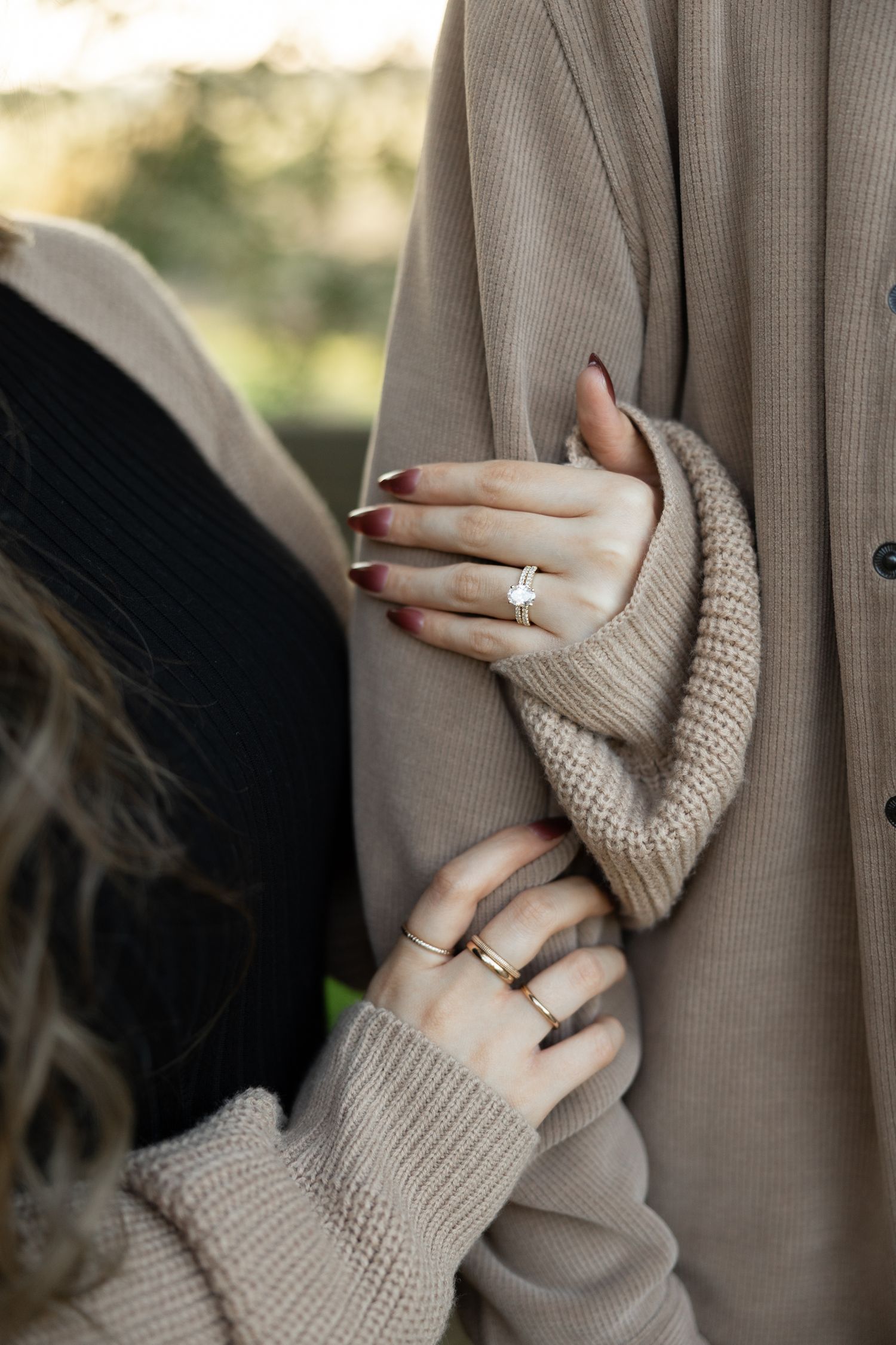 Close-up of hands with engagement ring holding onto a beige sweater sleeve.