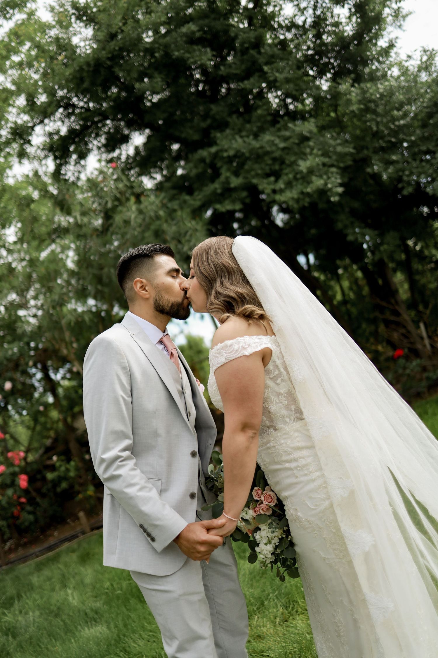 Romantic outdoor wedding portraits with couple embracing among lush greenery and trees.