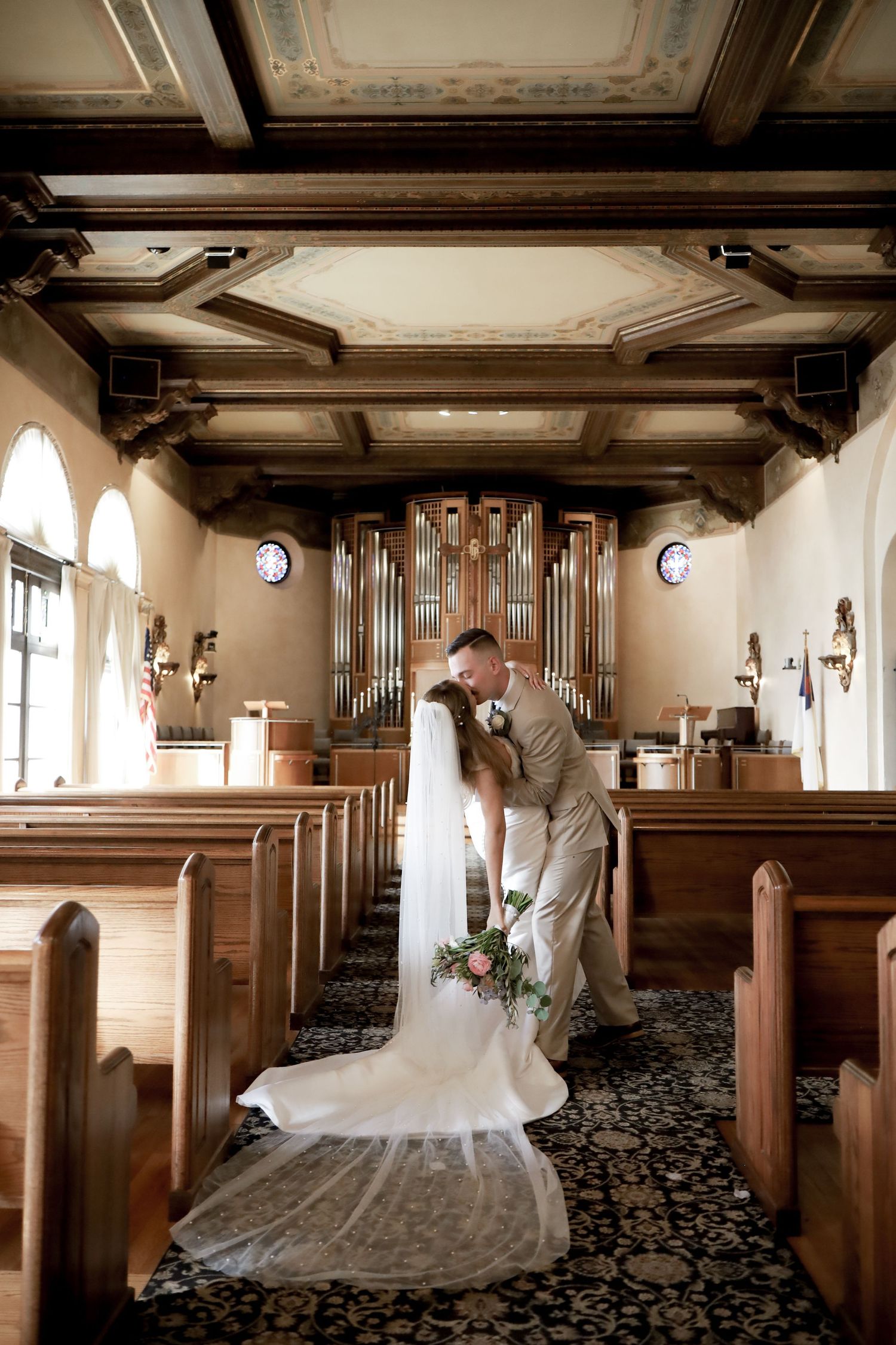 A couple shares an intimate moment in a church with ornate organ pipes and wooden pews.