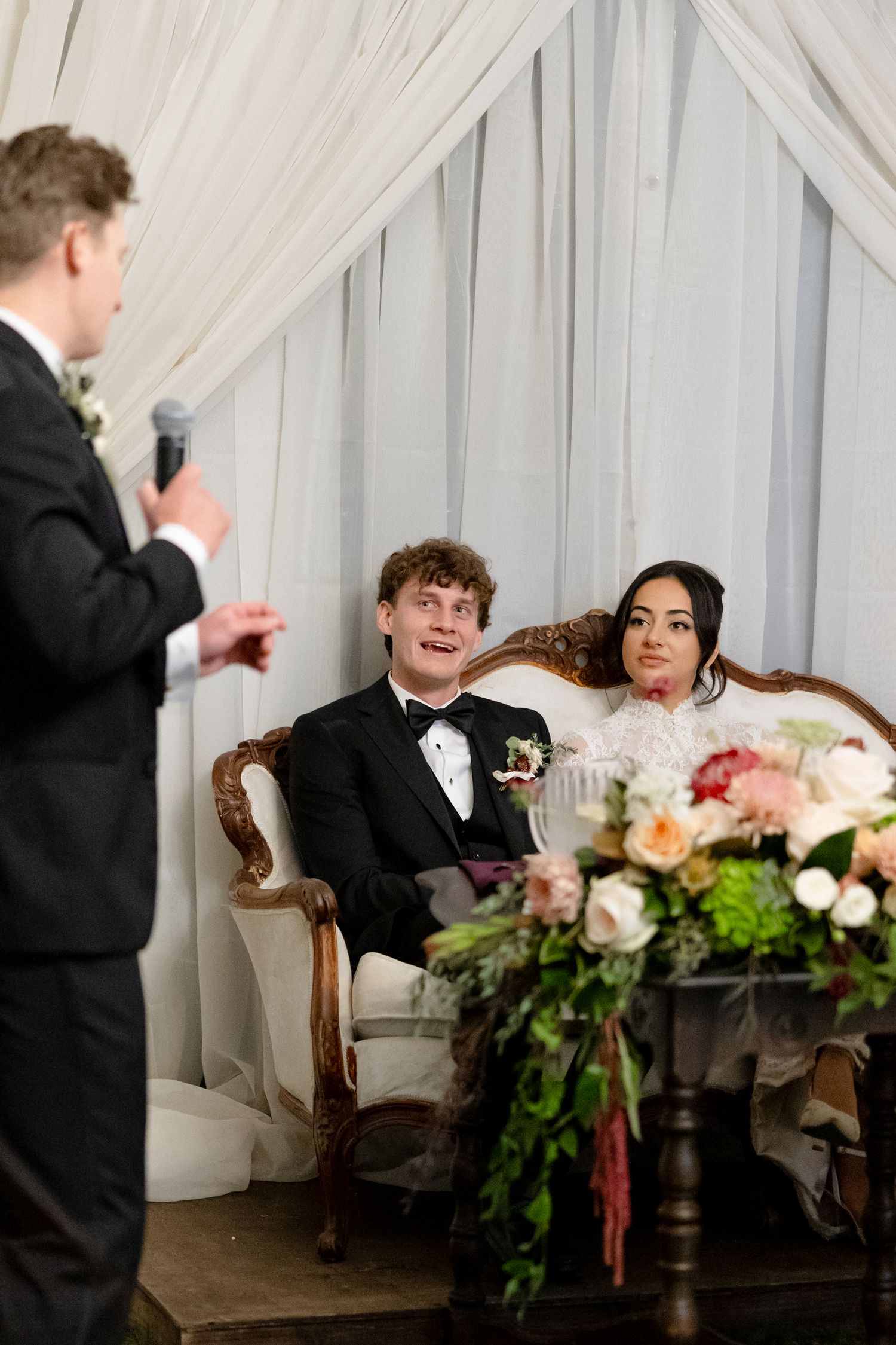 Bride and groom seated at sweetheart table listening to best man wedding speech.