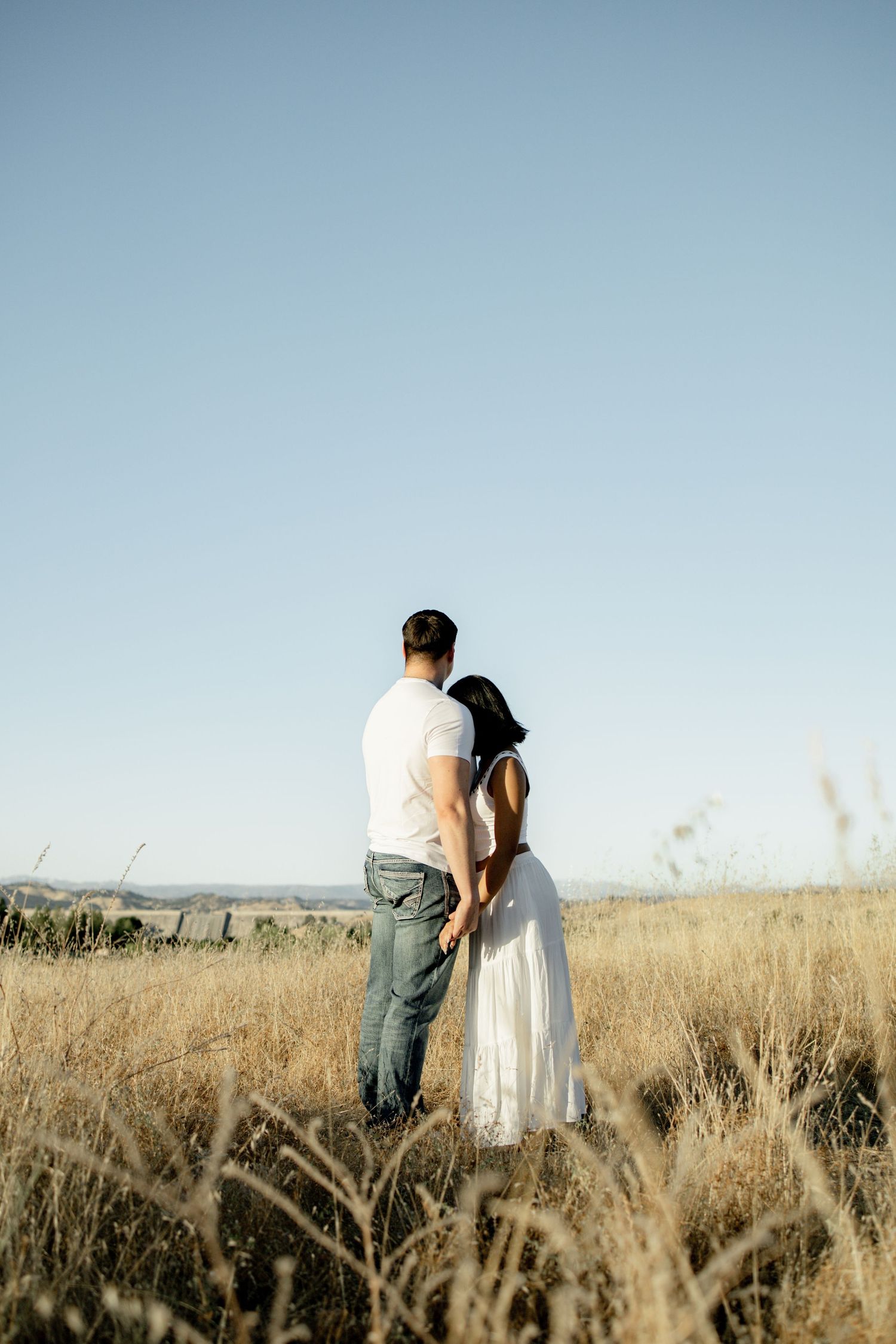 A couple sharing an intimate moment in a golden field against a blue sky.