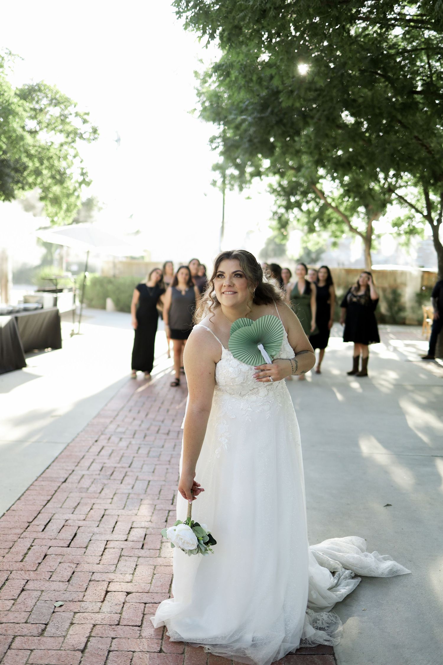 Wedding party in white dresses walking along brick pathway during outdoor celebration.