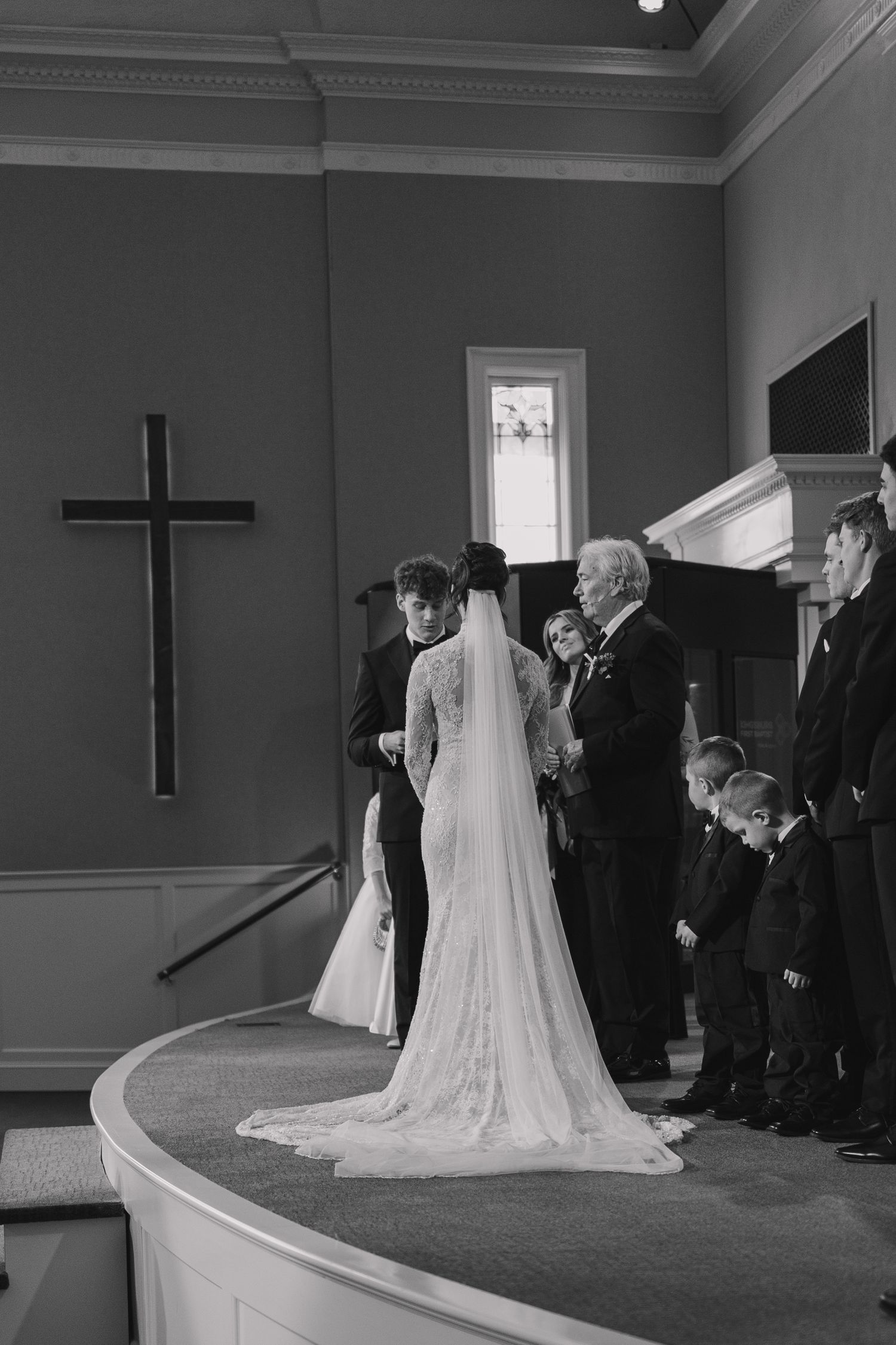 Black and white photo of a bride and groom exchanging vows at a church altar with a cross on the wall.