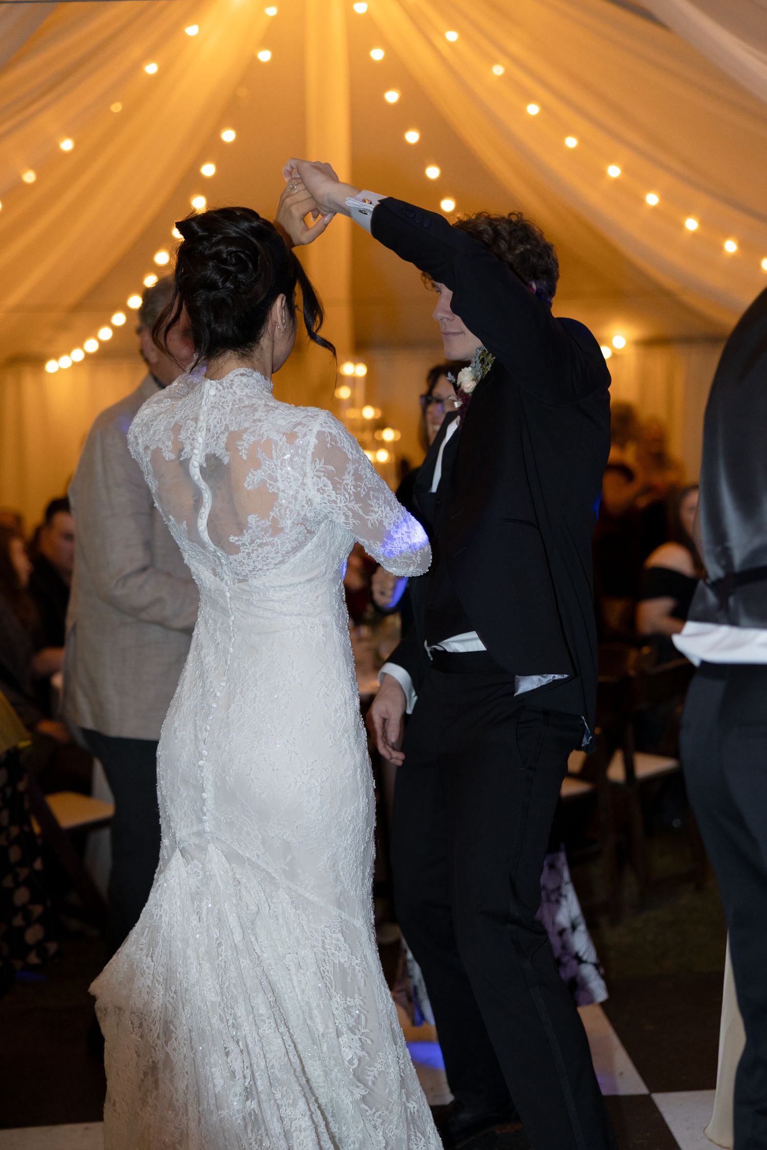 Bride and groom share first dance under warm string lights in a elegant tent wedding reception venue.