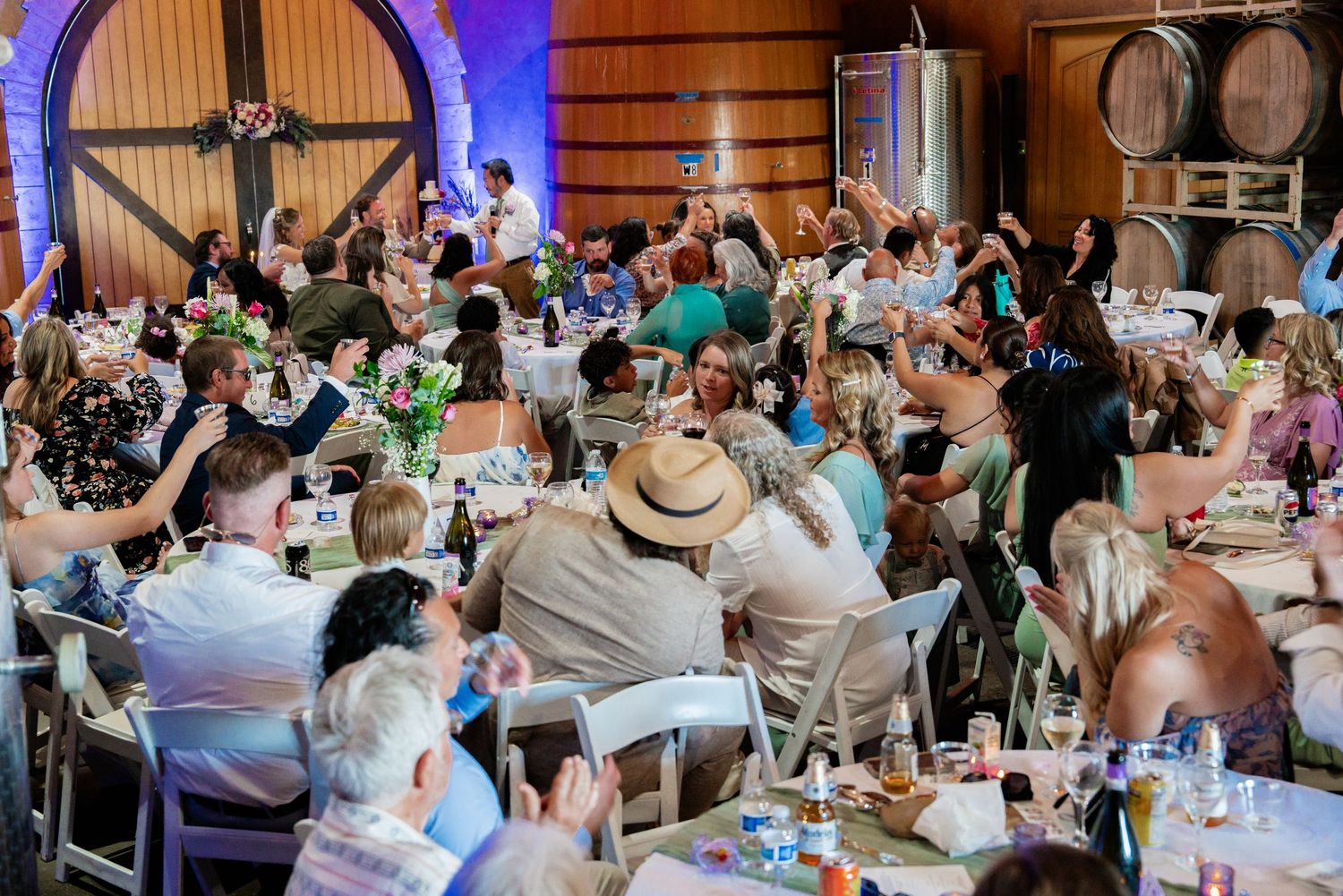 Guests celebrate at a lively winery event, raising glasses at decorated tables in a rustic barn venue.