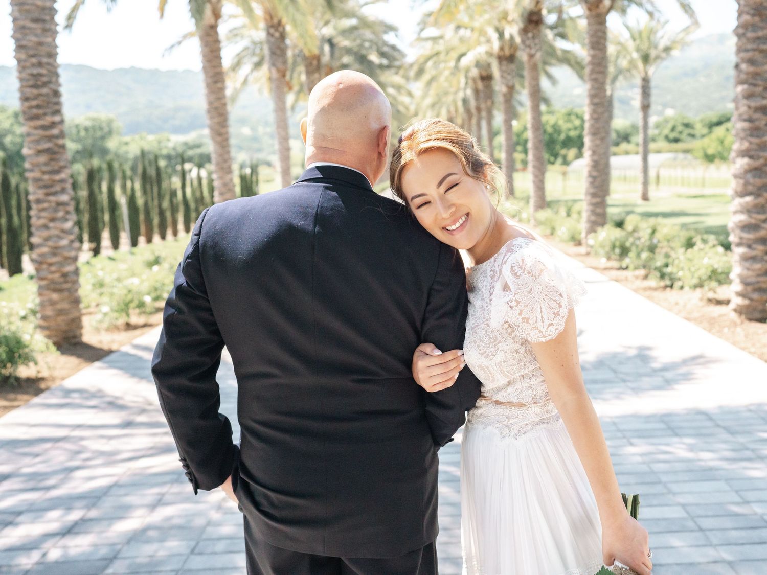 Romantic wedding photo on palm tree lined path with mountain backdrop.