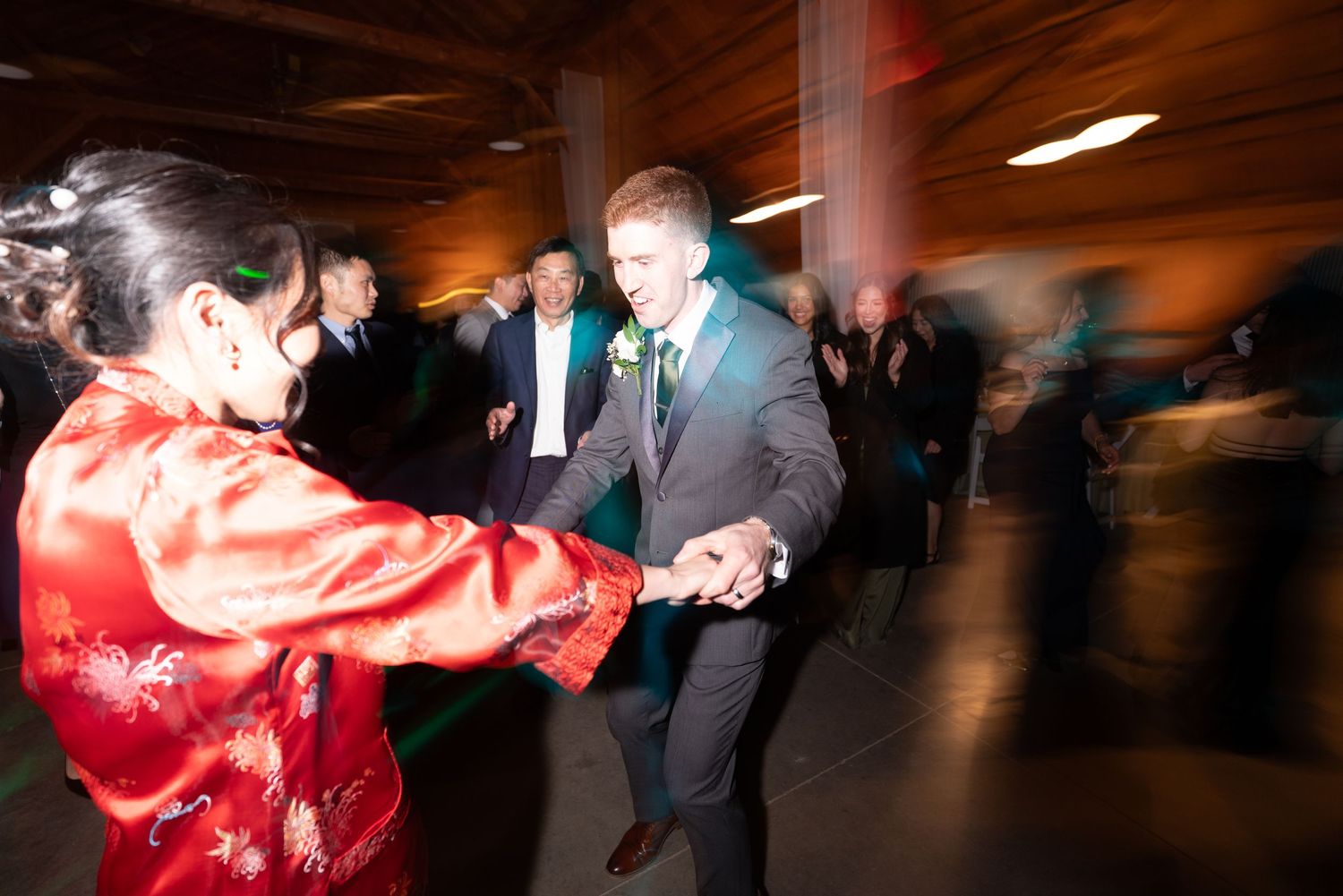A woman in a red Chinese qipao dances with a man in a gray suit at a festive wedding reception.