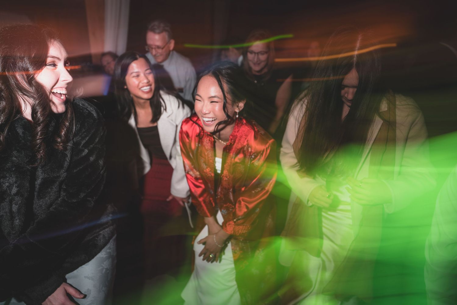 Group of friends dancing and laughing at a party with colorful green laser lights in the background.