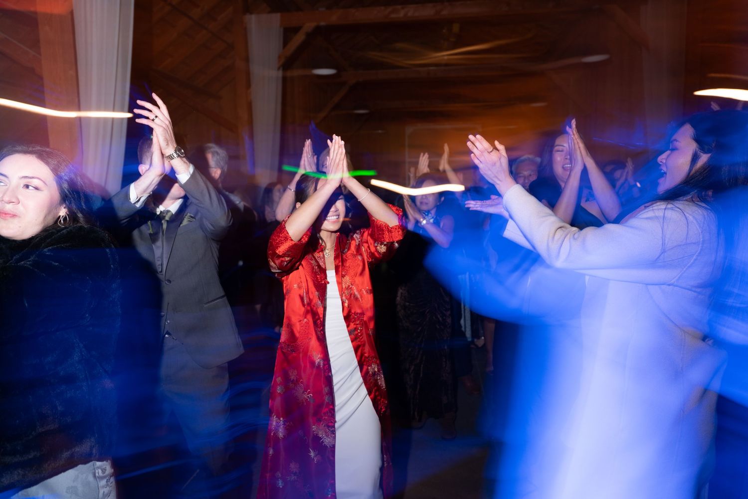 Guests dancing with hands raised at a lively wedding reception under blue and purple lights.