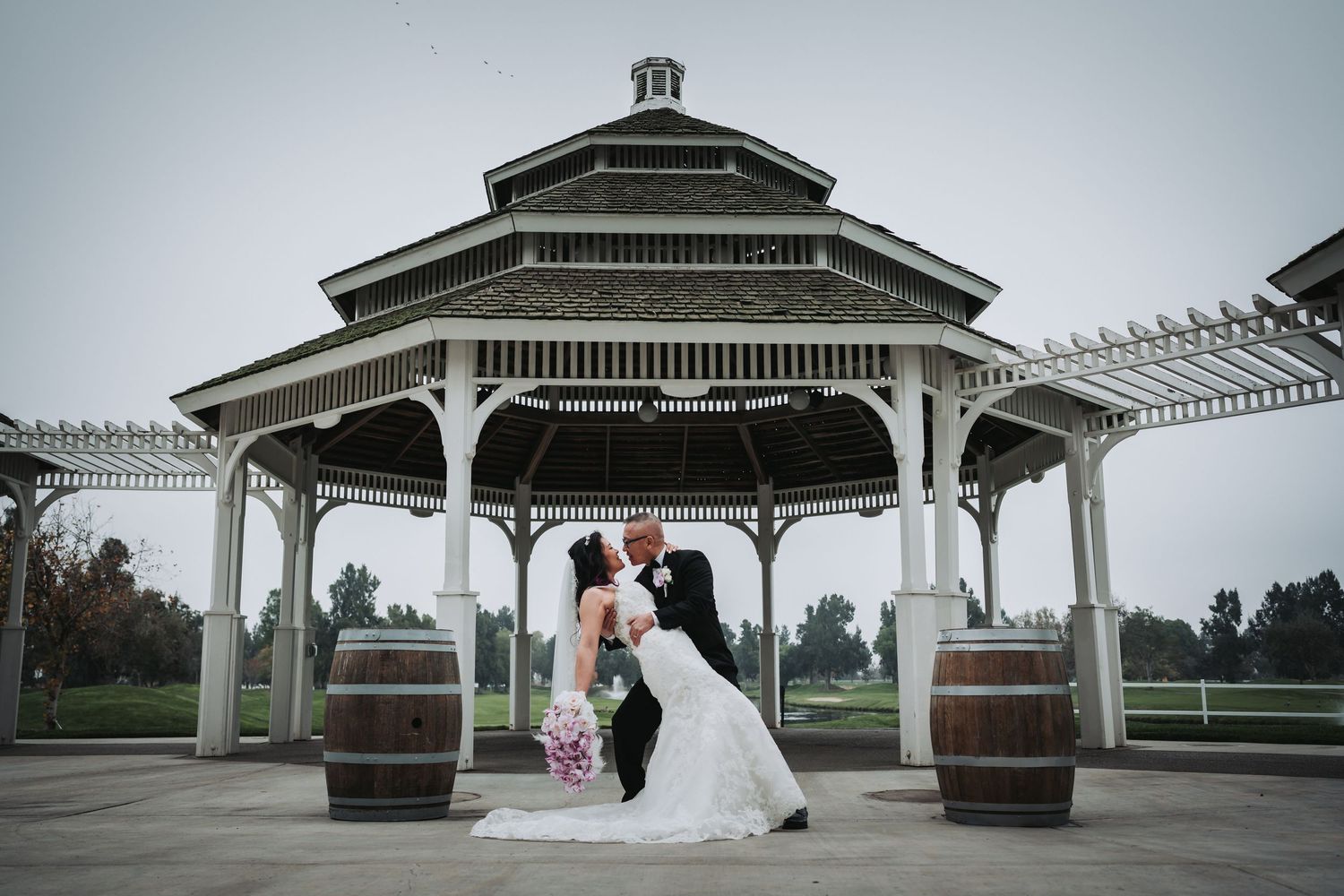 Bride and groom share a romantic kiss under a white gazebo on a golf course during their outdoor wedding ceremony.