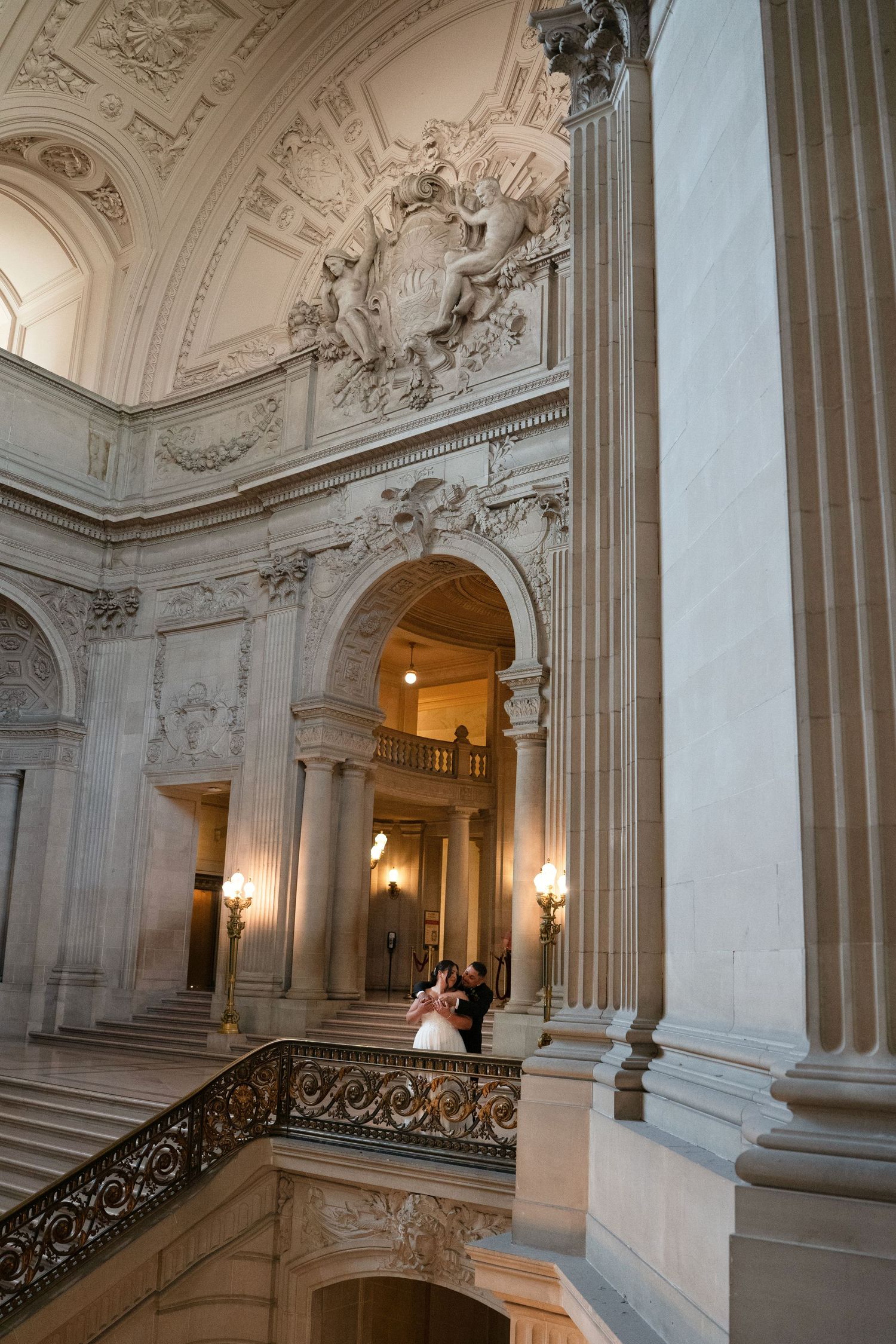Bride and groom pose on ornate grand staircase inside San Francisco City Hall's stunning Beaux-Arts marble interior.