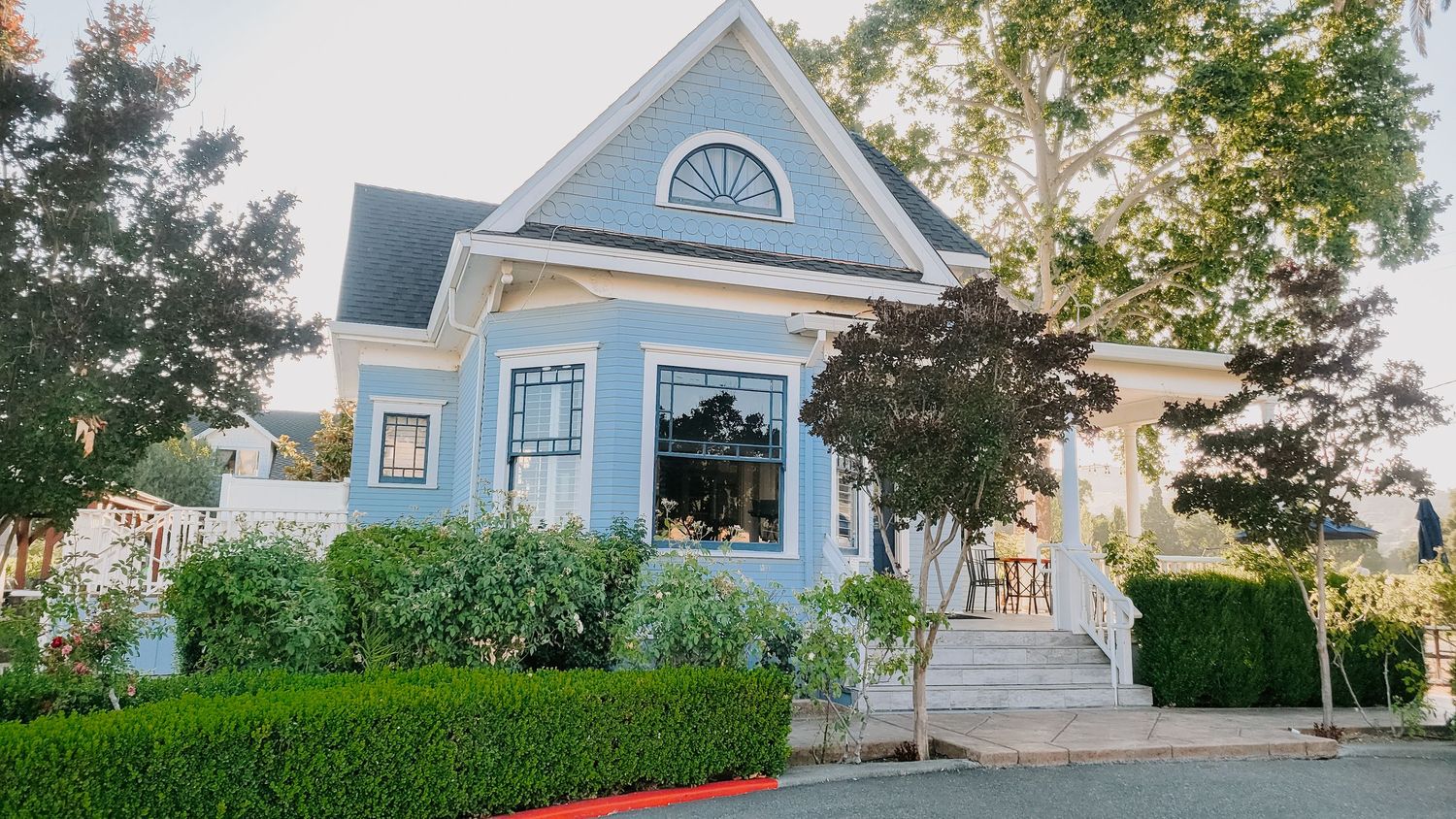 Beautiful blue Victorian mansion with white trim and manicured hedges in California style.