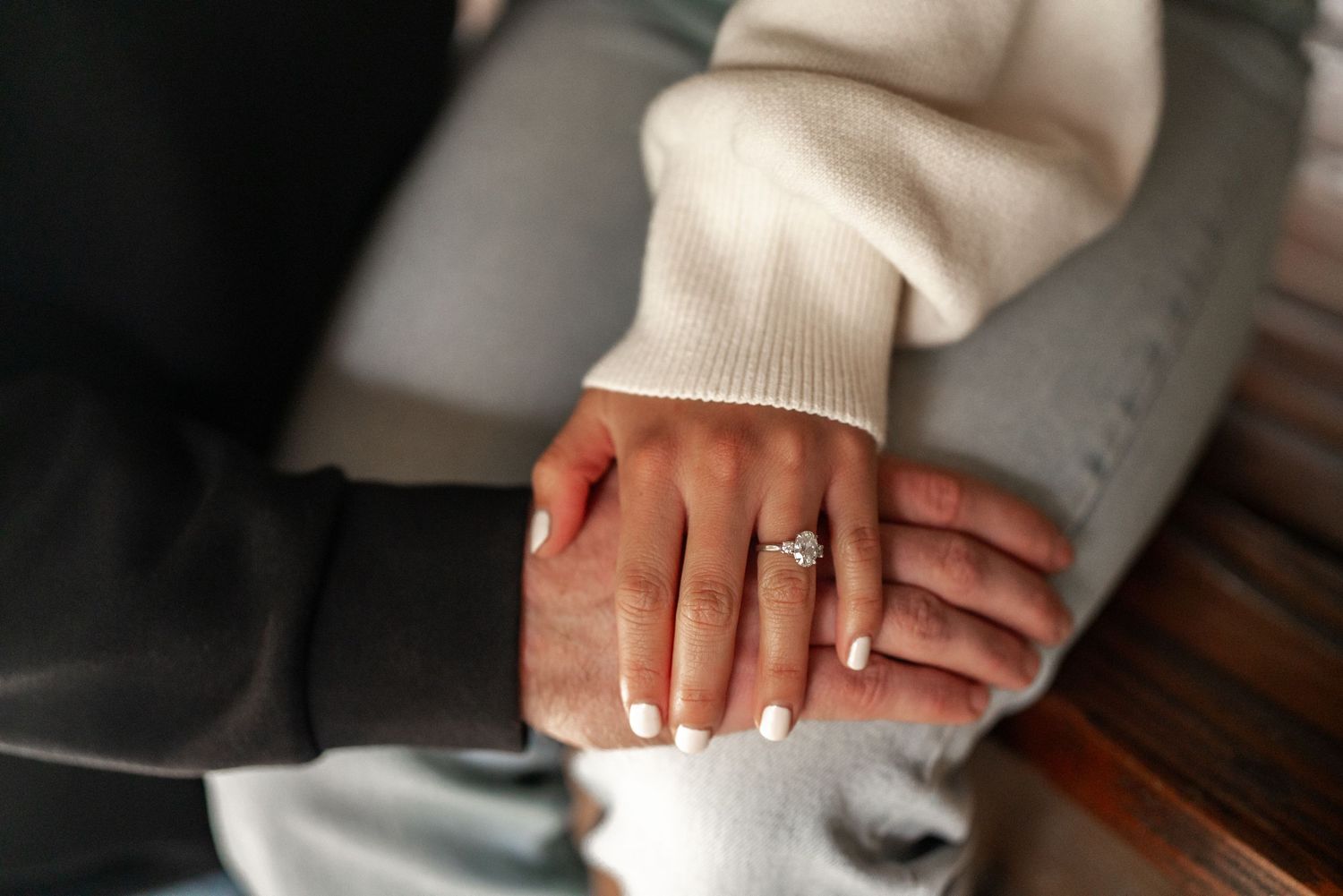 Close-up of hands displaying an engagement ring against a cream sweater.