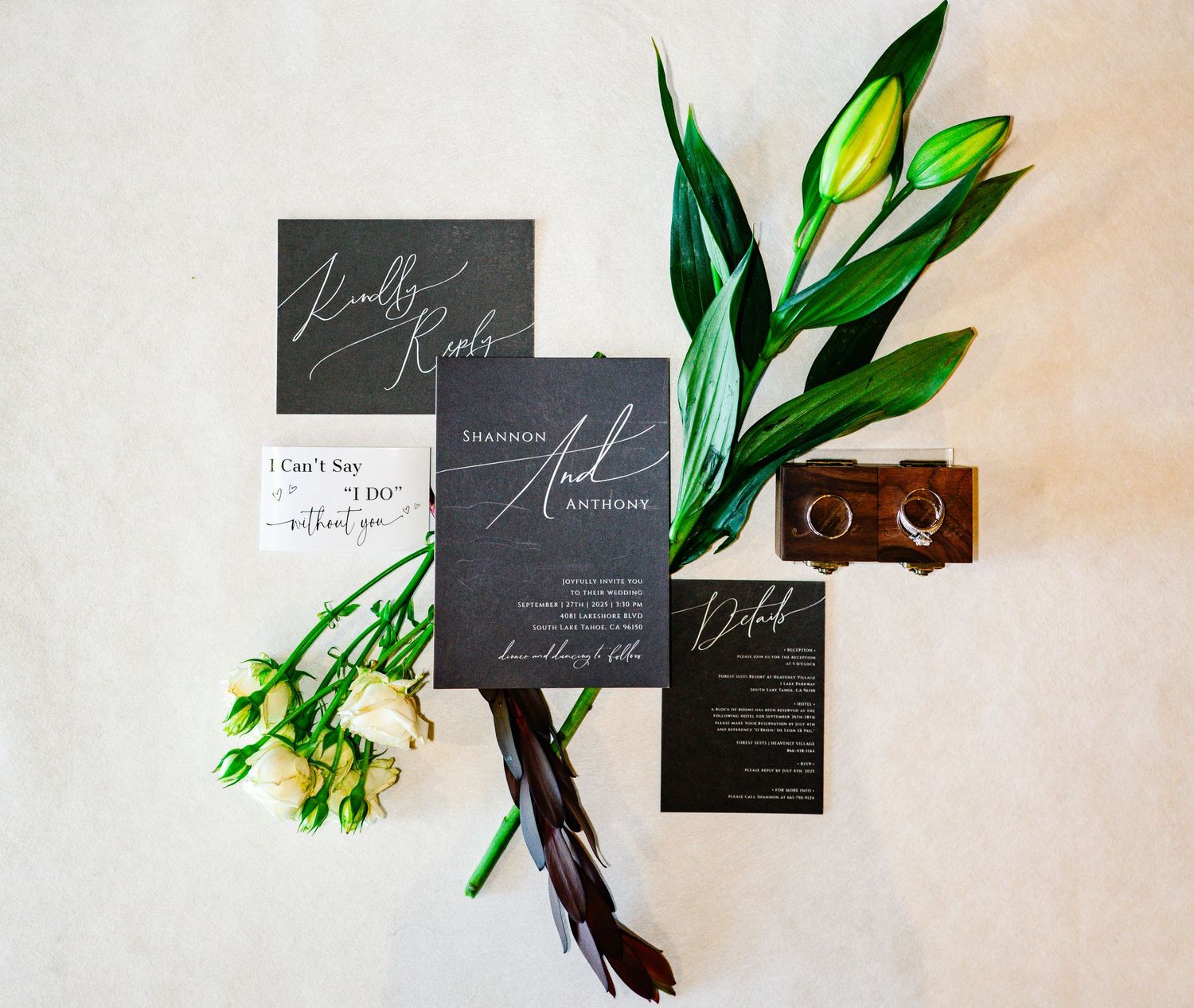 Elegant dark wedding invitation suite with white calligraphy, green tulips, feathers, and gold rings on white background.