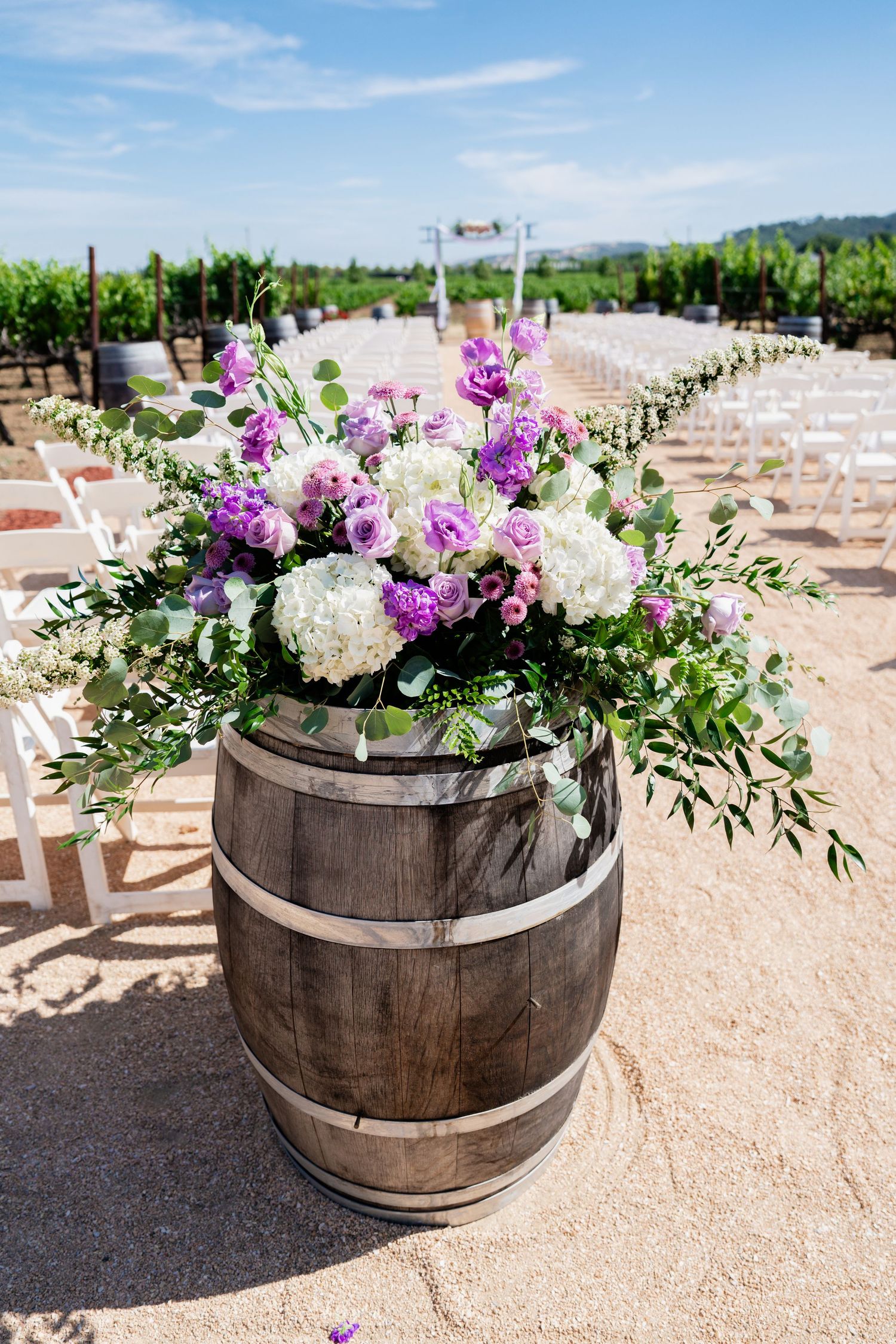 Rustic wine barrel planters filled with purple and white flowers decorating an outdoor venue. at Vezér Family Vineyard - Blue Victorian