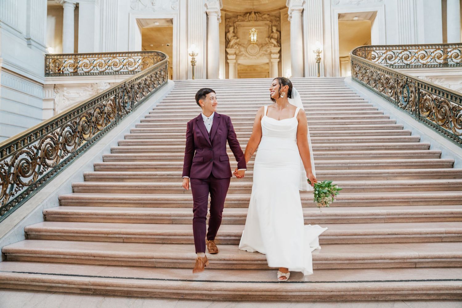 Couple walking up grand marble staircase with ornate railings.