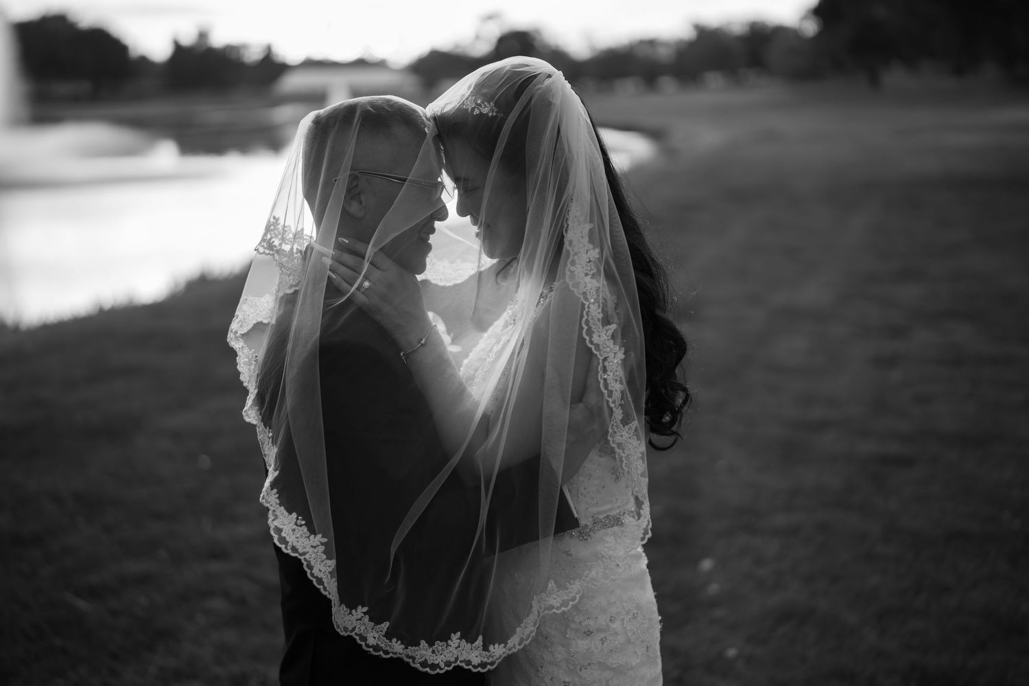 Black and white wedding photo of two brides sharing an intimate moment under a lace veil outdoors.