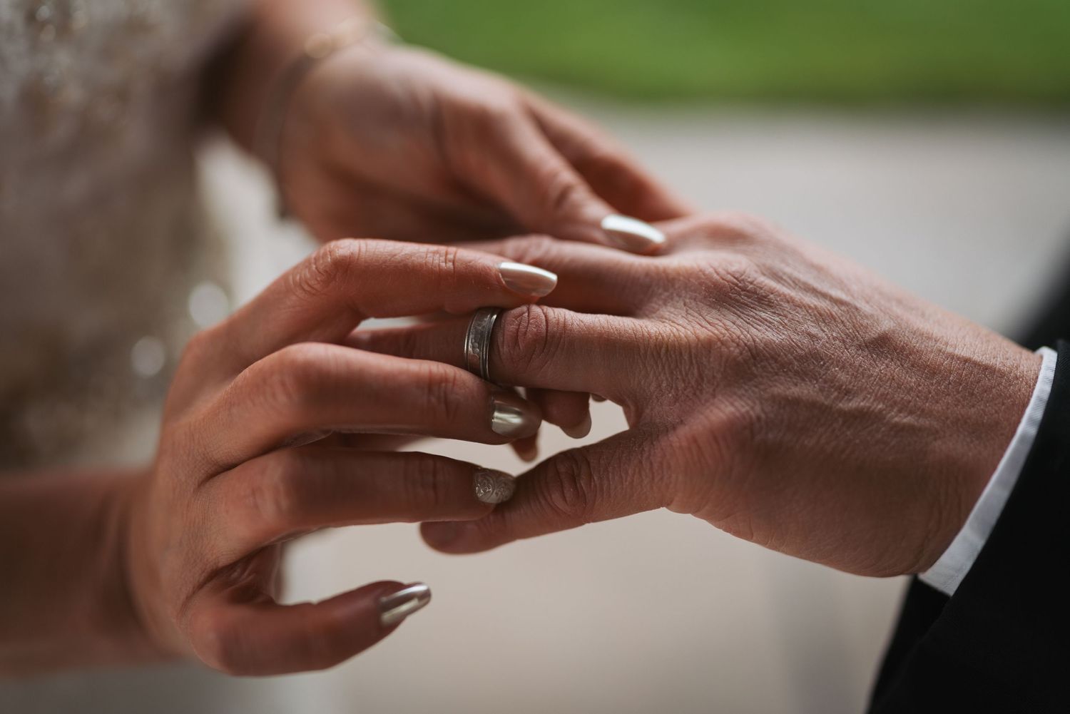 Close-up of a bride placing a black wedding band on the groom's finger during a wedding ring exchange ceremony.